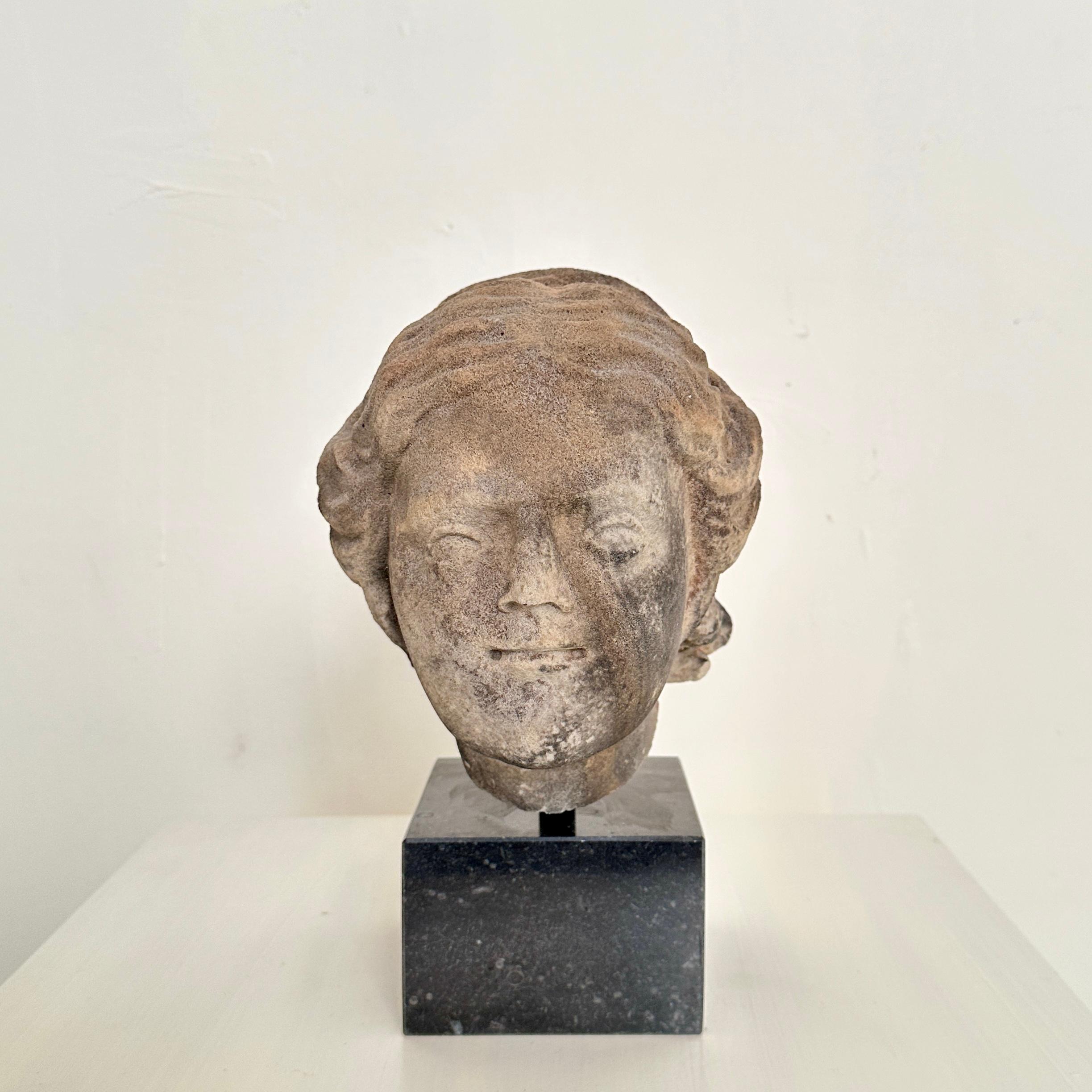 Dating back to around 1780, this 18th-century Baroque Grey Hand-Carved Sandstone Head of a Woman is a remarkable testament to the artistry of its era. The intricately crafted piece, resting on a marble base, captures the essence of Baroque