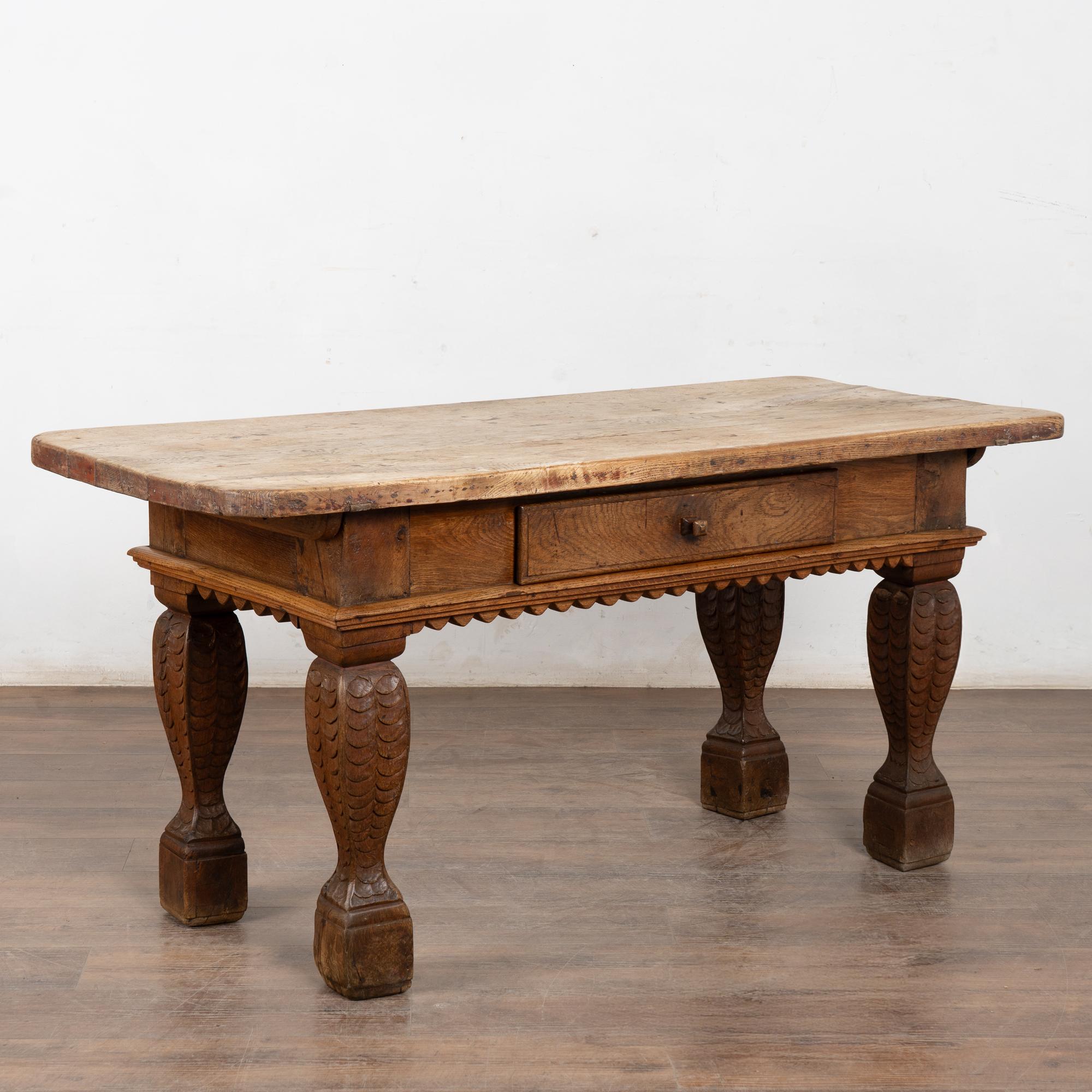 This handsome baroque style oak library table with one drawer has heavily turned and carved legs with scalloped skirt.
The top is all natural (lighter) oak with nicks, gouges, cracks and stains reflecting generations of use, likely as a work