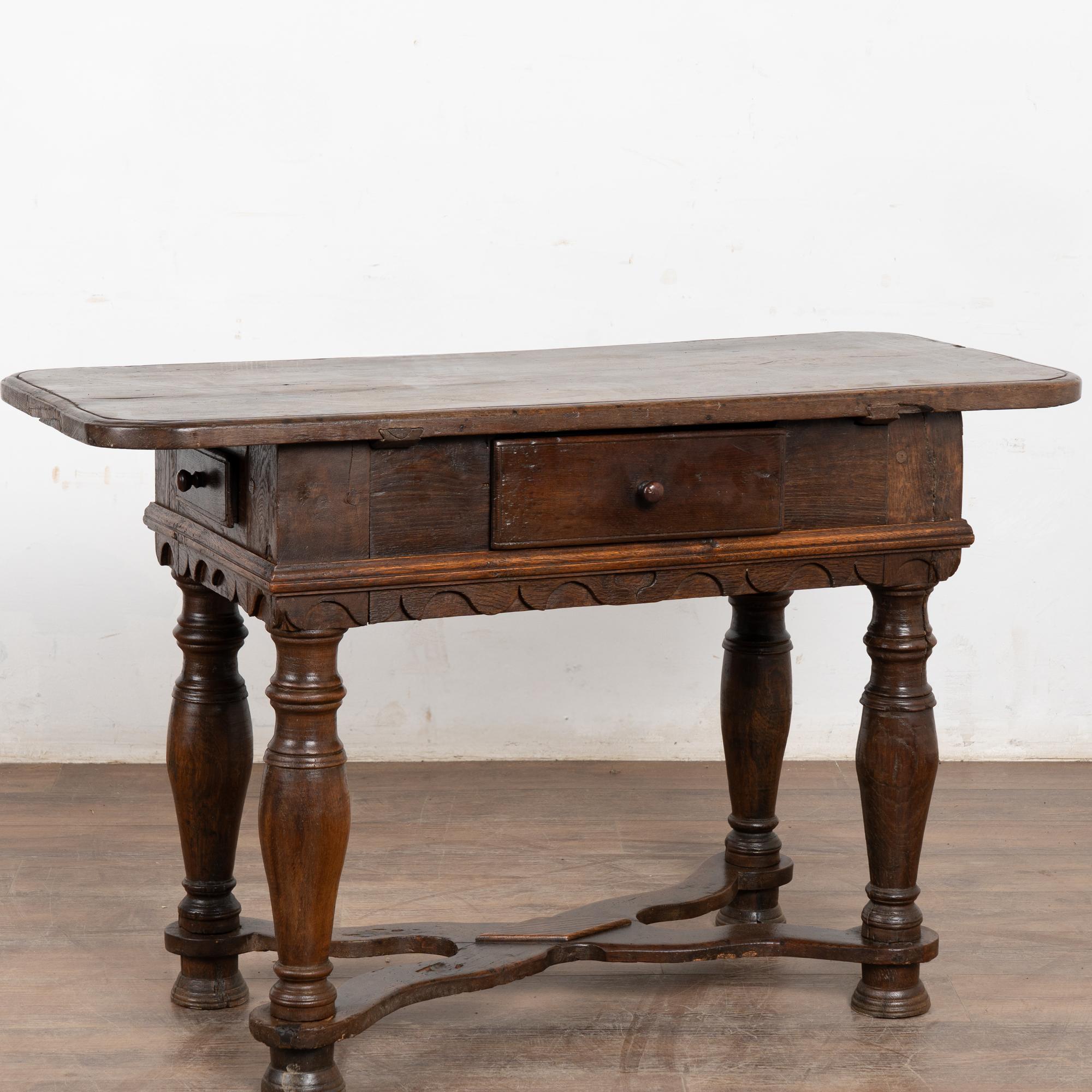 This handsome baroque oak side table with three functioning drawers has heavy turned legs and an attractive X lower stretcher.
Note the dark patina of the top; distress from 200 years of use are revealed in the multiple cracks, dark stains,