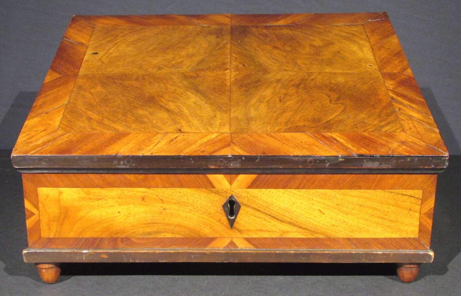 La superficie esterna è decorata con suggestivi pannelli geometrici di impiallacciature di legno chiaro e scuro a contrasto con modanature ebanizzate, la parte superiore inclinata si apre su cerniere di ferro successive per un interno semplice che