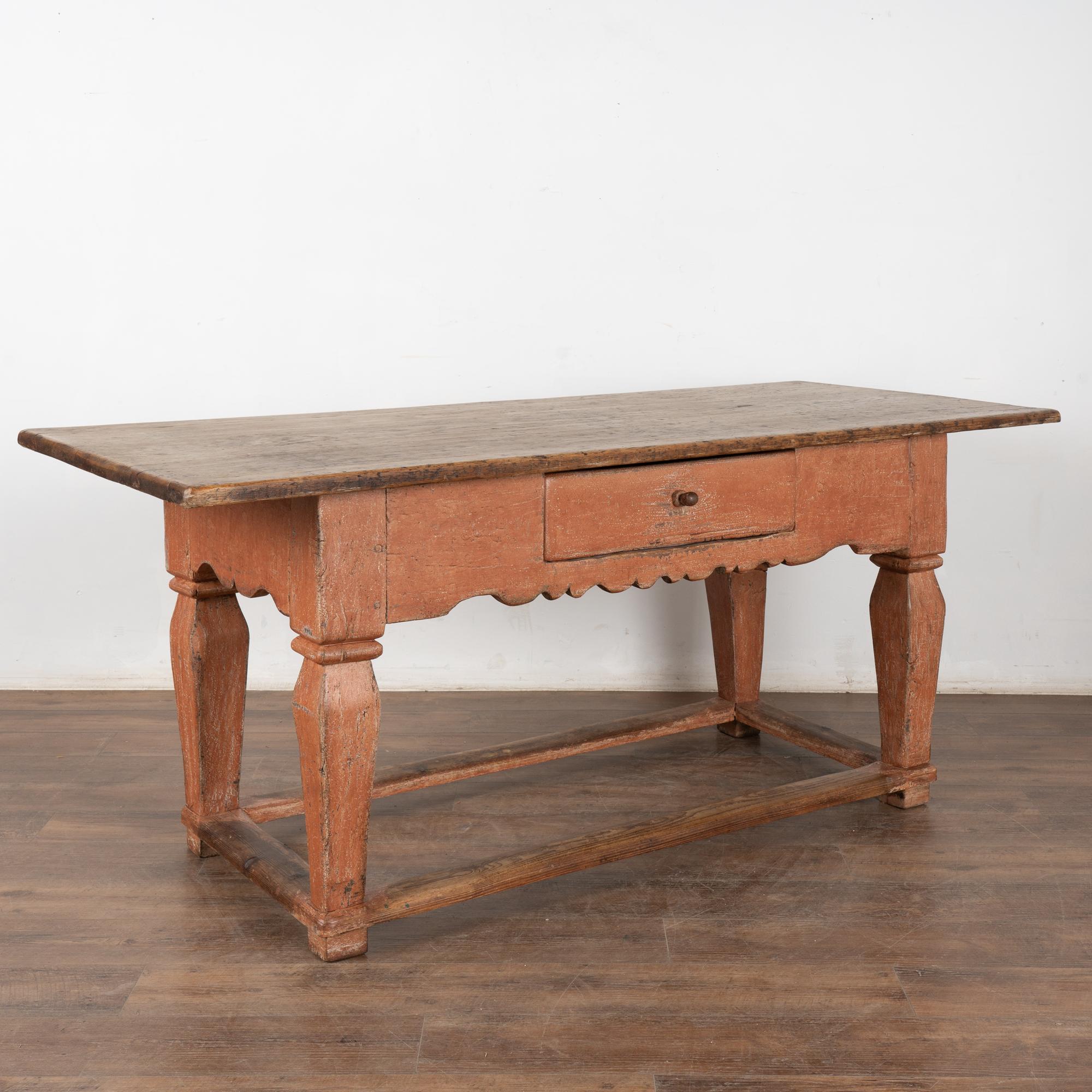 This handsome baroque oak library table with one drawer has heavily turned legs, scalloped skirt and lower stretchers.
The original painted finish of the base is worn and distressed; the aged patina has softened the brick red/salmon colored finish