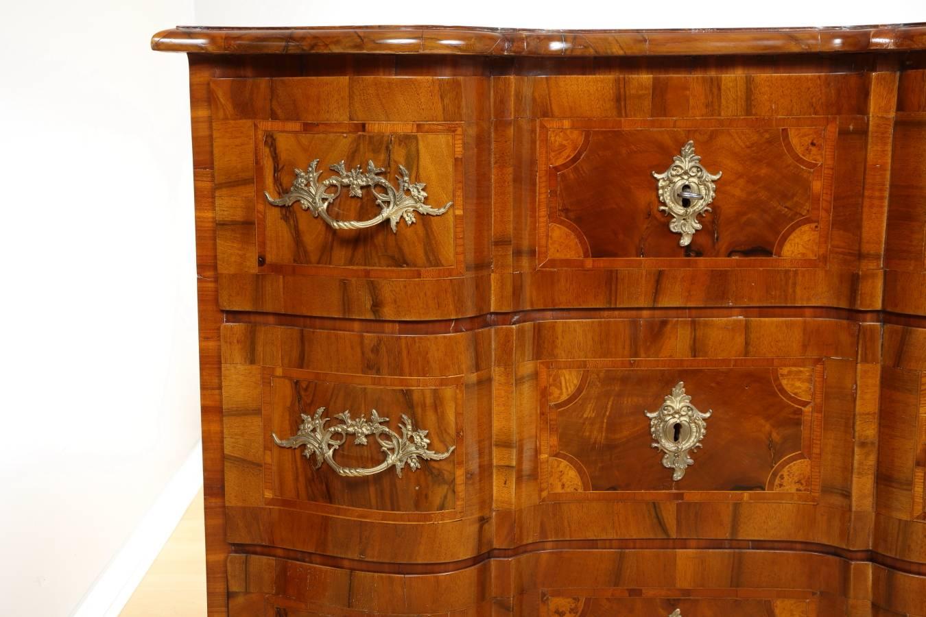 18th century Baroque walnut commode. Magnificent Baroque walnut chest of drawers with scalloped front, crafted in South Germany Baroque period. The piece is inlaid with various veneers including birch, rose, walnut, and black oak. Three drawers with