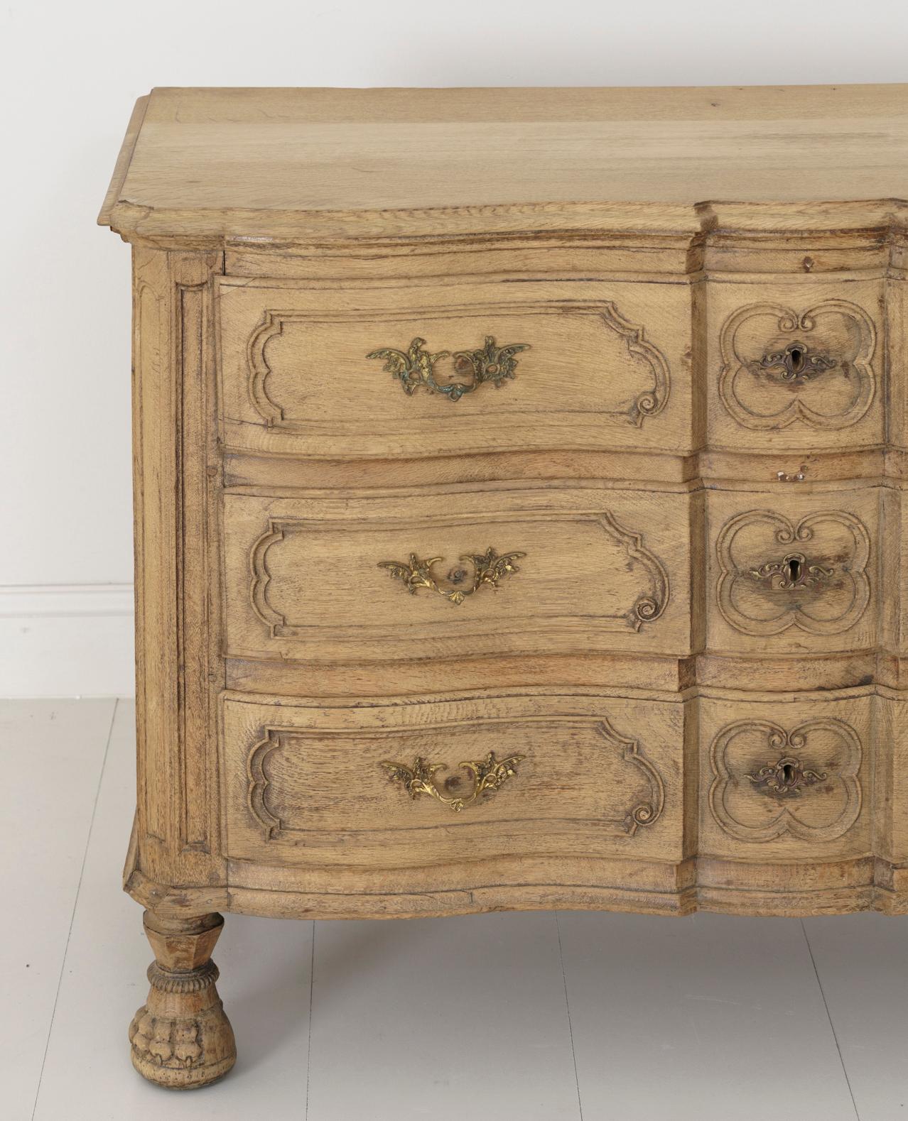 A richly carved Louis XVI period bleached oak commode with an Arbalette shaped front and paw feet. Original brass hardware. From Liege, Belgium, circa 1780.