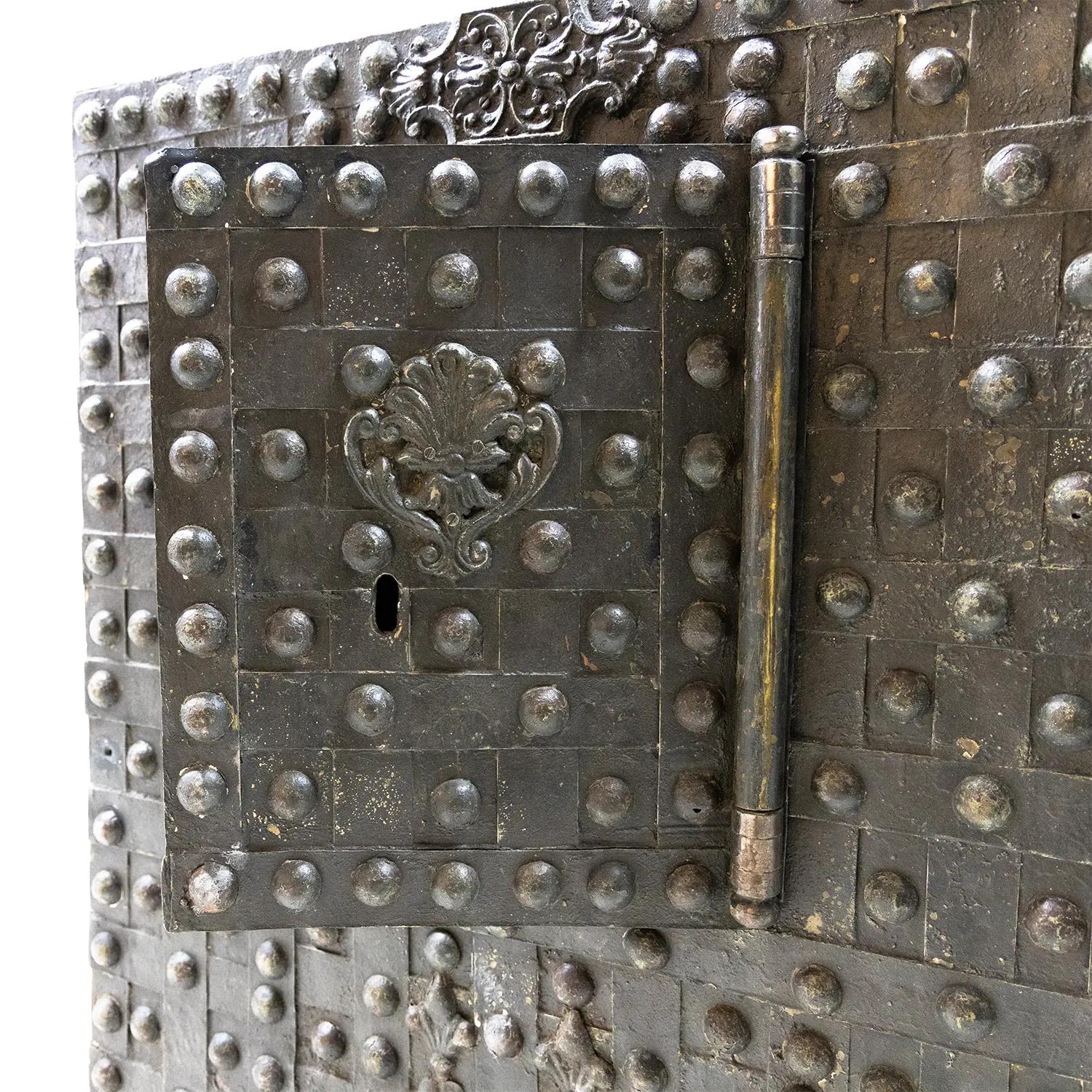 A large, antique single-door safe or cassa forte made of hand crafted iron with rivets and bands on the surface and palmettes and rocaille decorations on the front, in good condition. The decor piece is consisting its original metal hardware and