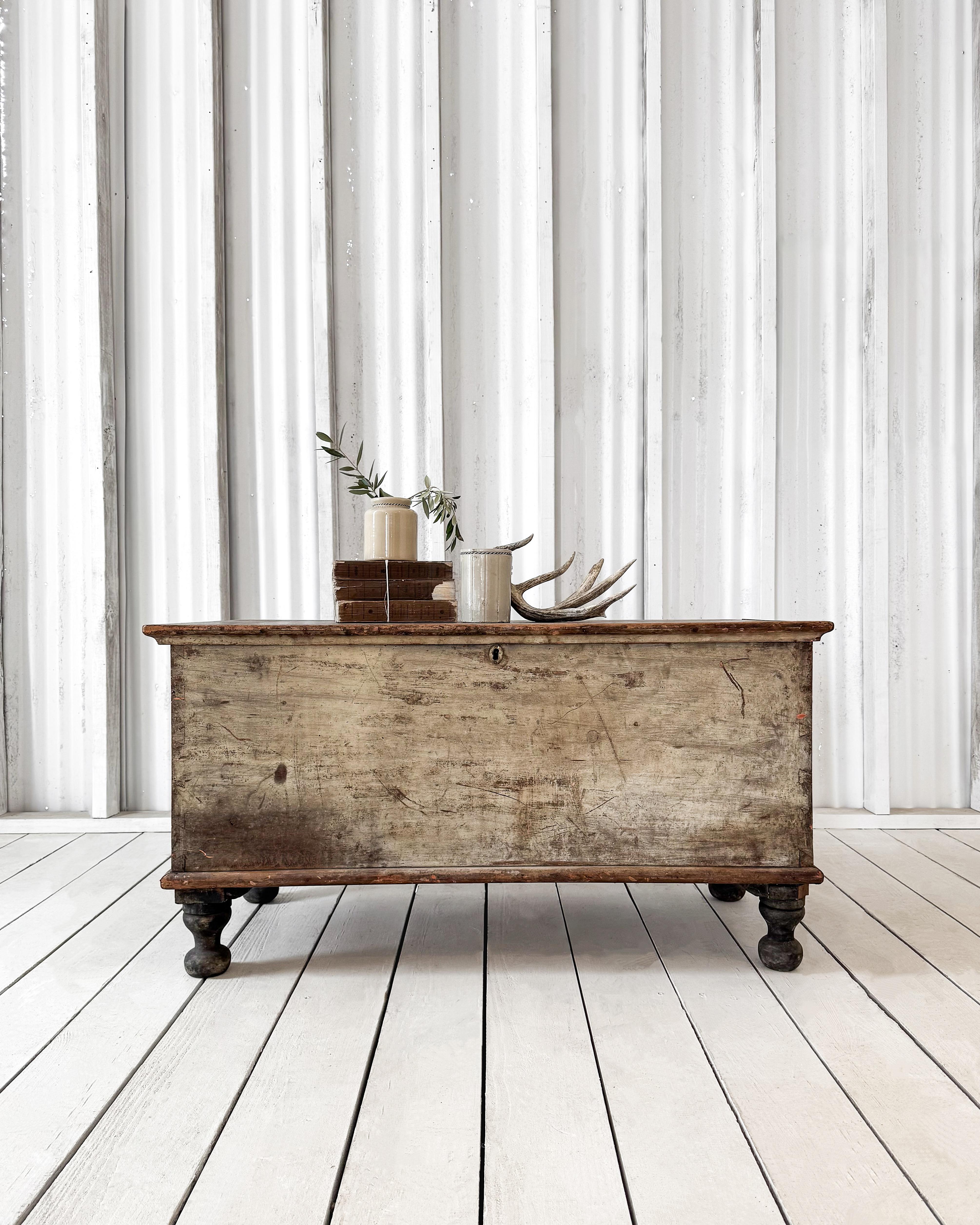 A wonderfully preserved blanket chest showcasing a timeless blend of form and function. Its original warm white and earthy-toned paint is beautifully worn, revealing the rich history of the piece. Crafted with dovetailed construction for durability,