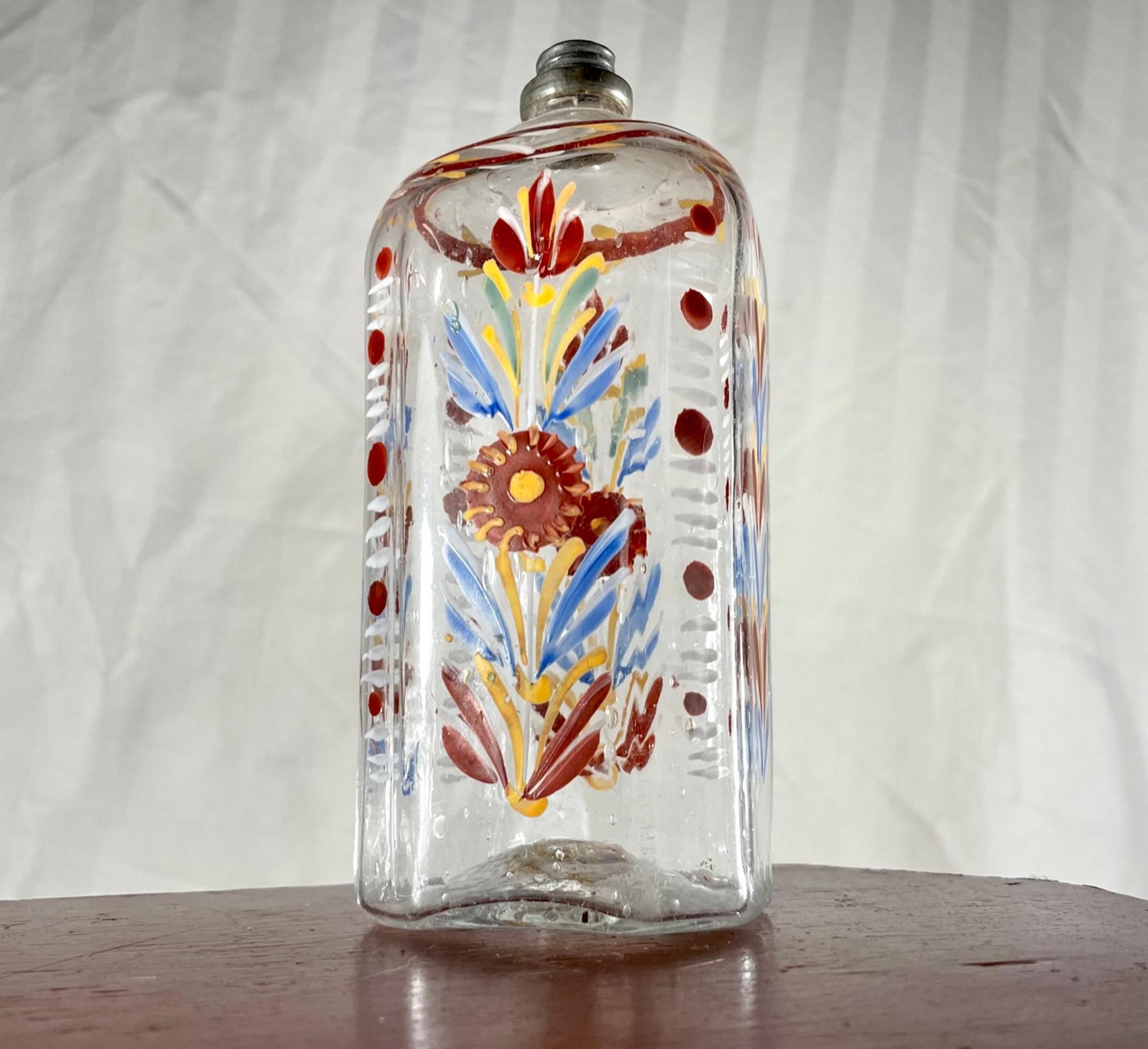 18th Century Blown Glass Enameled Stiegel Type Flask.

Folk art hand blown, and hand enameled polychrome decorated Stiegel colorless glass flask. Origin is probably 18th century Bohemia.  The bottle has a rectangular base with cut corners and has a