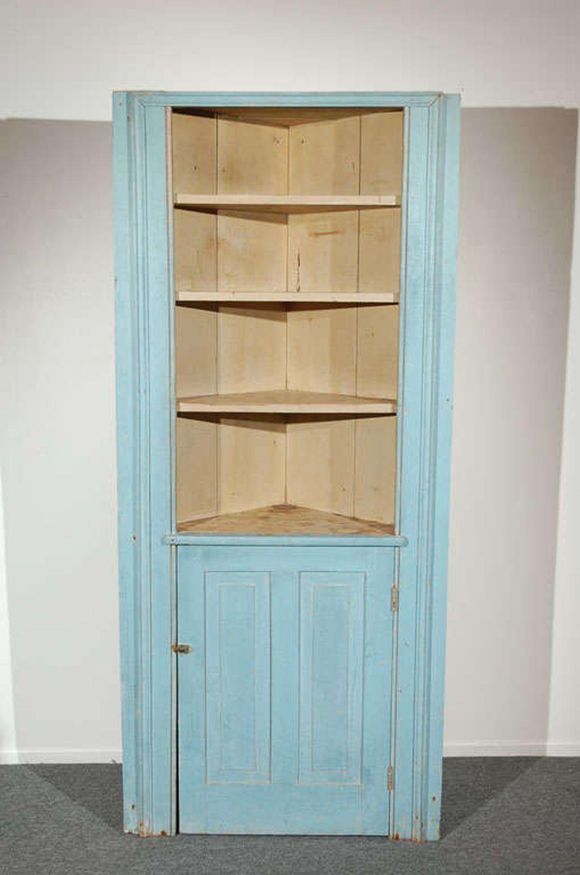 Cette armoire d'angle bleue en deux parties présente un extérieur peint en dégradé et un intérieur peint en blanc lavé.  L'extérieur peint en bleu est recouvert d'une sous-couche peinte en blanc.  Il y a deux portes en verre au-dessus de la base de