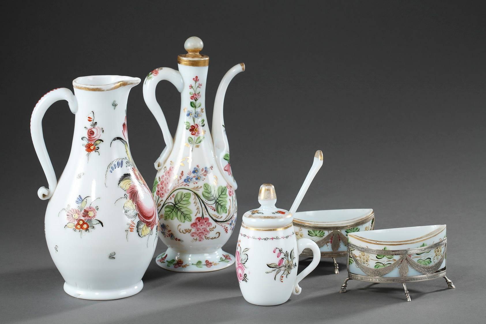 White opaline service set composed of a pitcher, a coffee pot, a mustard pot, and two salt cellars. They are decorated with enameled bouquets of flowers and highlighted with gilded bands. The salt cellars rest in gilded mounts that are decorated