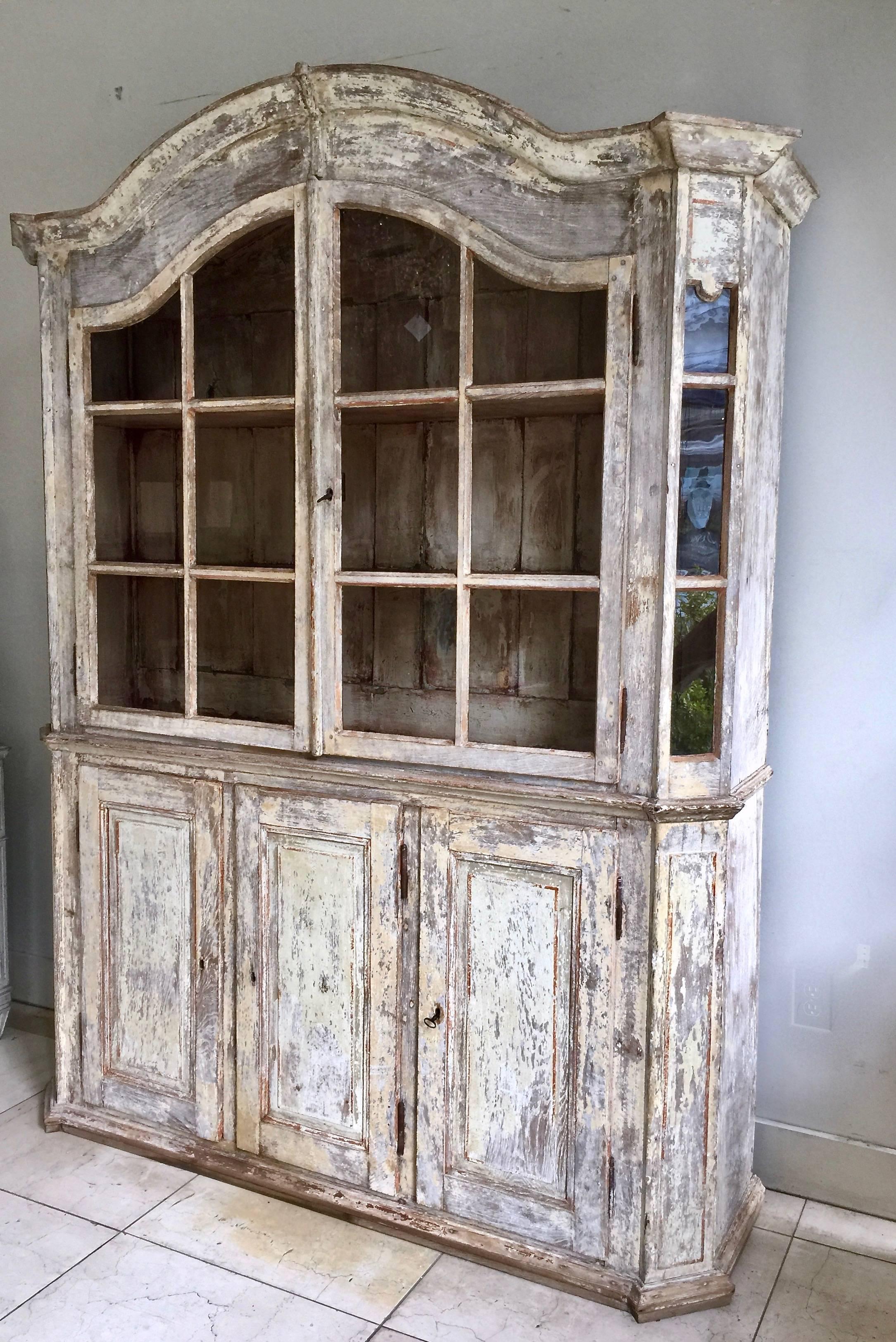 A very handsome 18th century French bookcase/vitrine cabinet in impressive scale with arched pediment cornice and panelled doors on three door cabinet base with bank of drawers inside of the middle section - all in time worn original patina.
Here