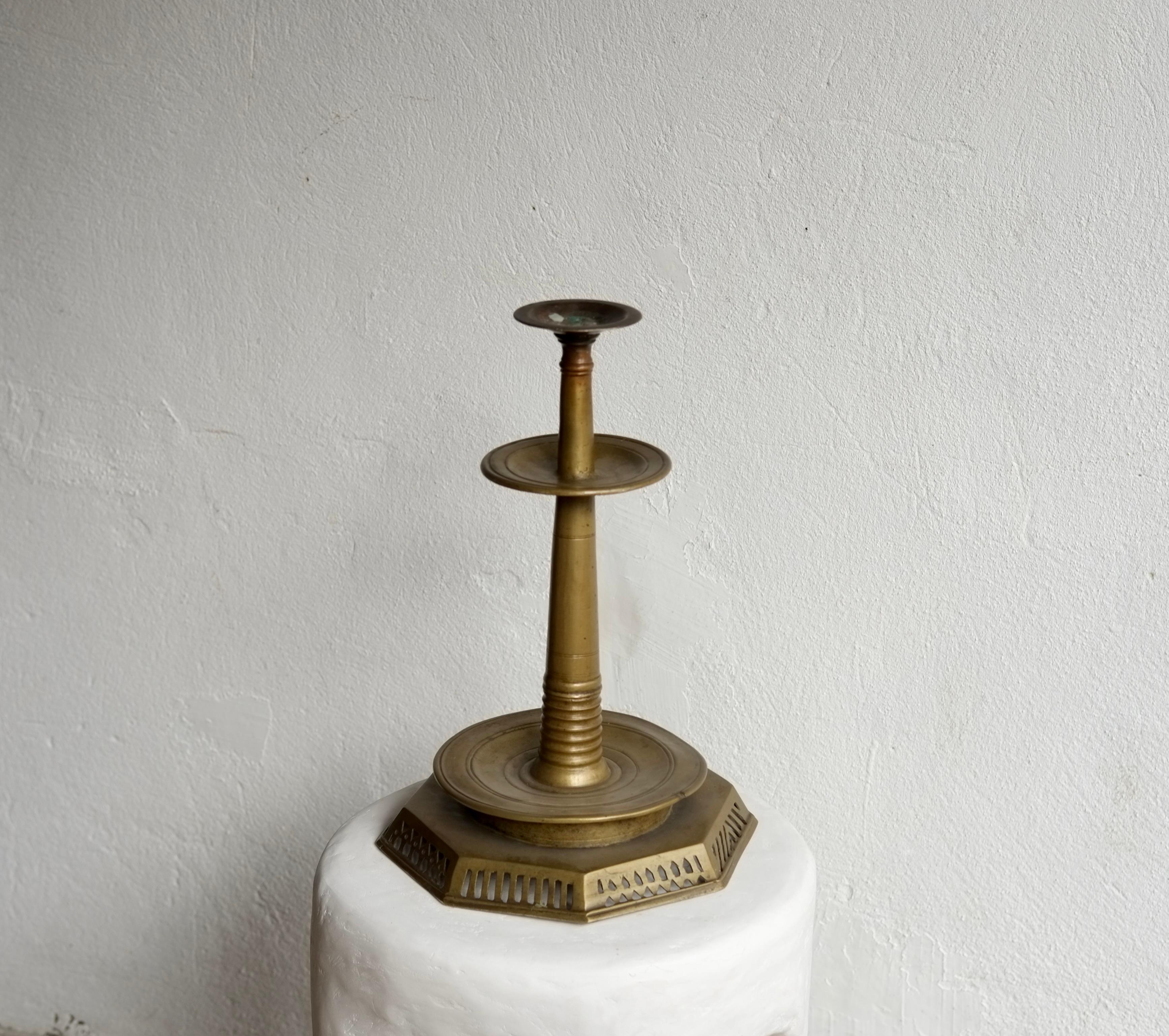 A large 18th century brass candlestick with an unusual geometric shaped pierced drip pan and two tier stem. 