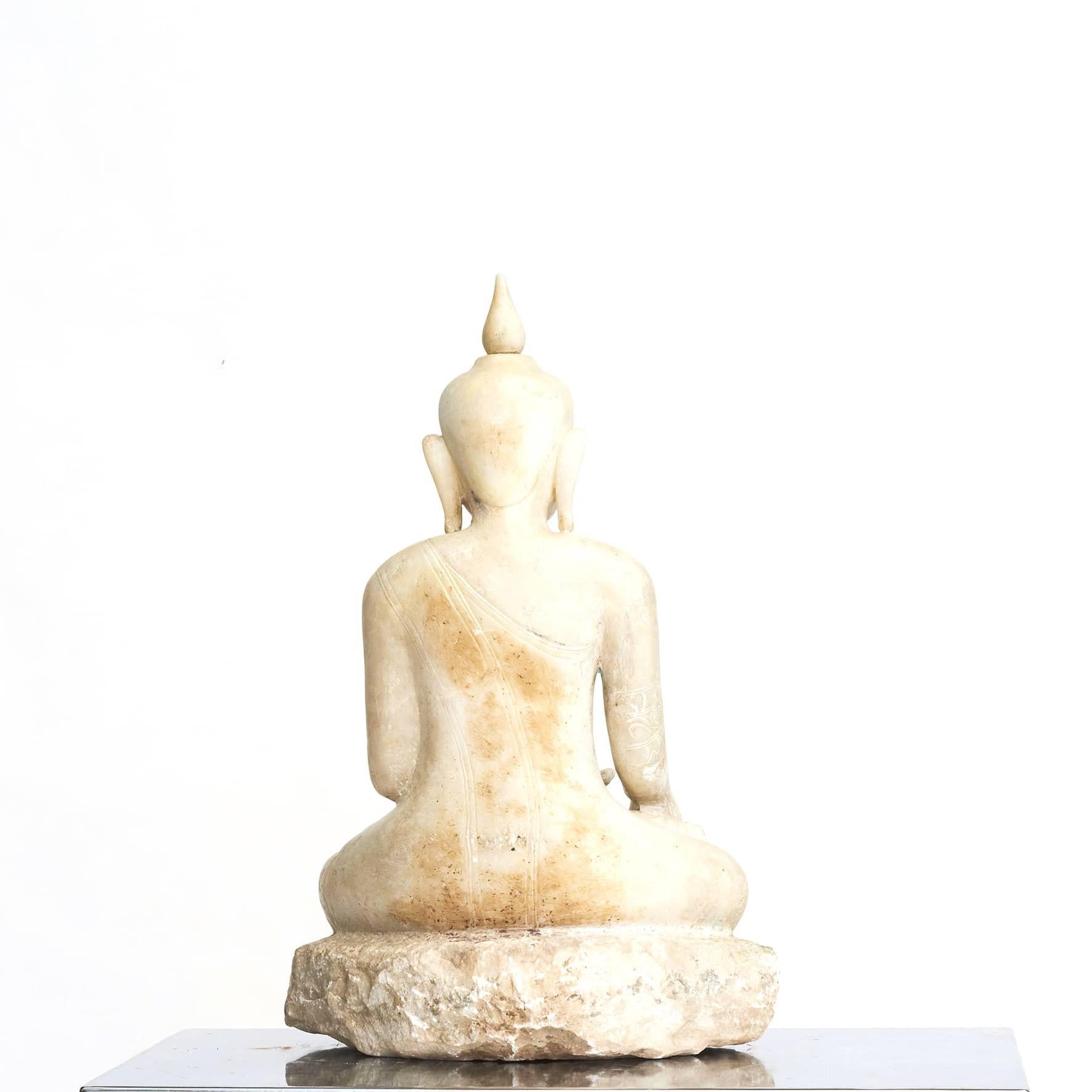A Burmese alabaster stone Buddha seated in Bhumisparsha mudra position (“calling the earth to witness”).
Many delicate carved details and a meditative face adorned with a slight smile and half-closed eyes.
The Buddha has traditional elongated