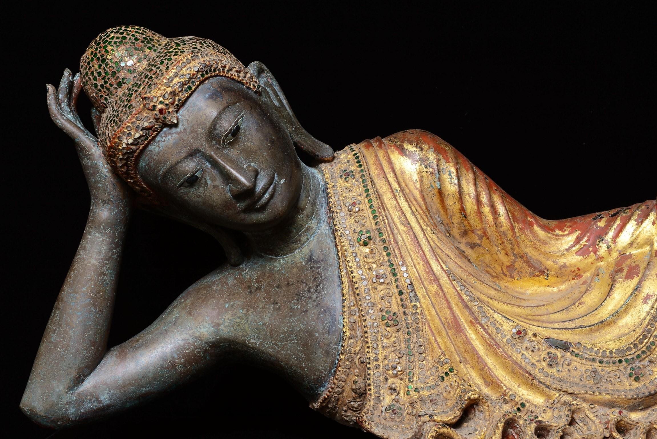 Very fine gilt bronze reclining Buddha.
The exquisite bronze reclining Buddha draped in a robe with meticulously forged folds of fabric, decorated with coloured glass and leaving the right shoulder exposed, his head supported by his right hand, his