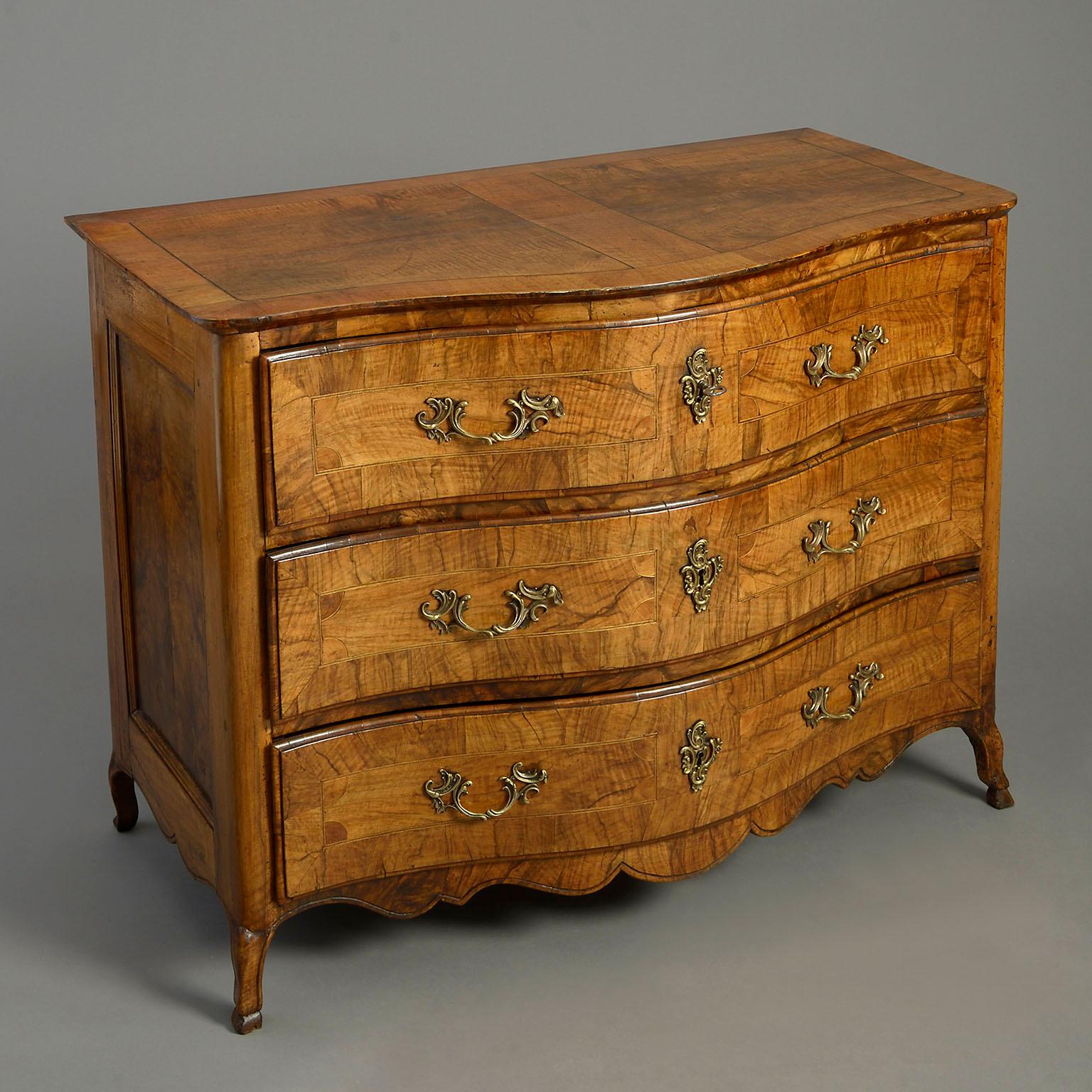 A late 18th century burr walnut parquetry commode, the overhanging top and three drawers with panelled inlay, mounted with rococo brass lock escutcheons and handles and raised on stylised hoof feet.