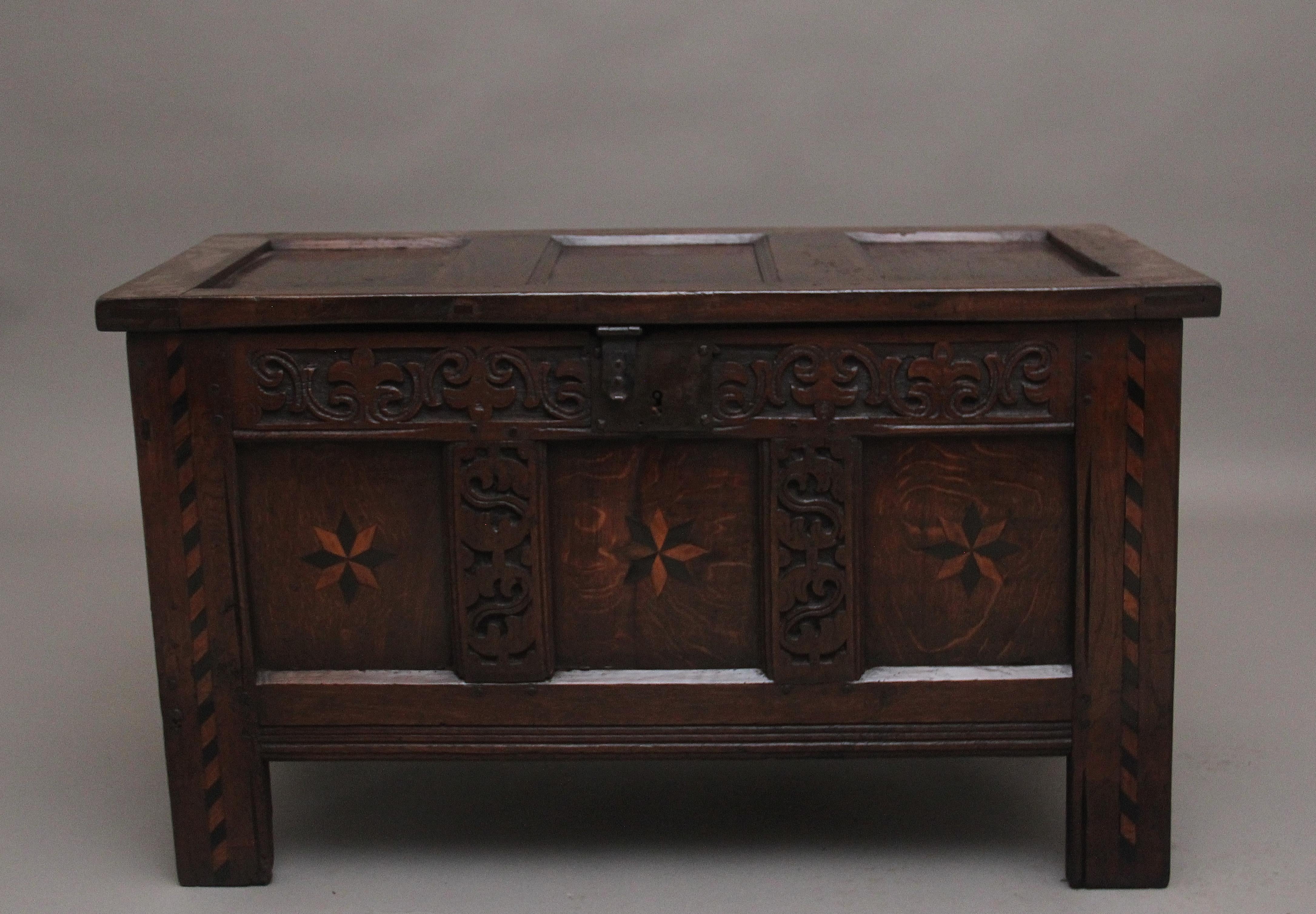 Early 18th Century carved and inlaid oak coffer, having a hinged three panelled top opening to reveal a large compartment space, the three panelled front having wonderful decorative carving,  two tone star inlay on each panel with decorative