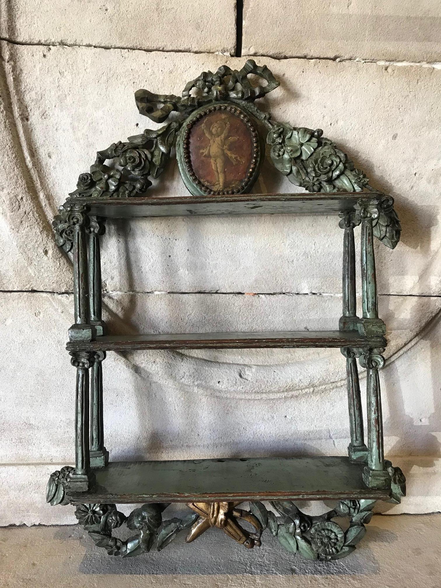 Hand carved and hand painted hanging wall shelf. The beautiful carvings of a dancing Wreath of flowers and acanthus leaves, a Ribbon and bow with a finial at the bottom of flames flambeau. A painted Angelo putti surrounded by delicate carved beads