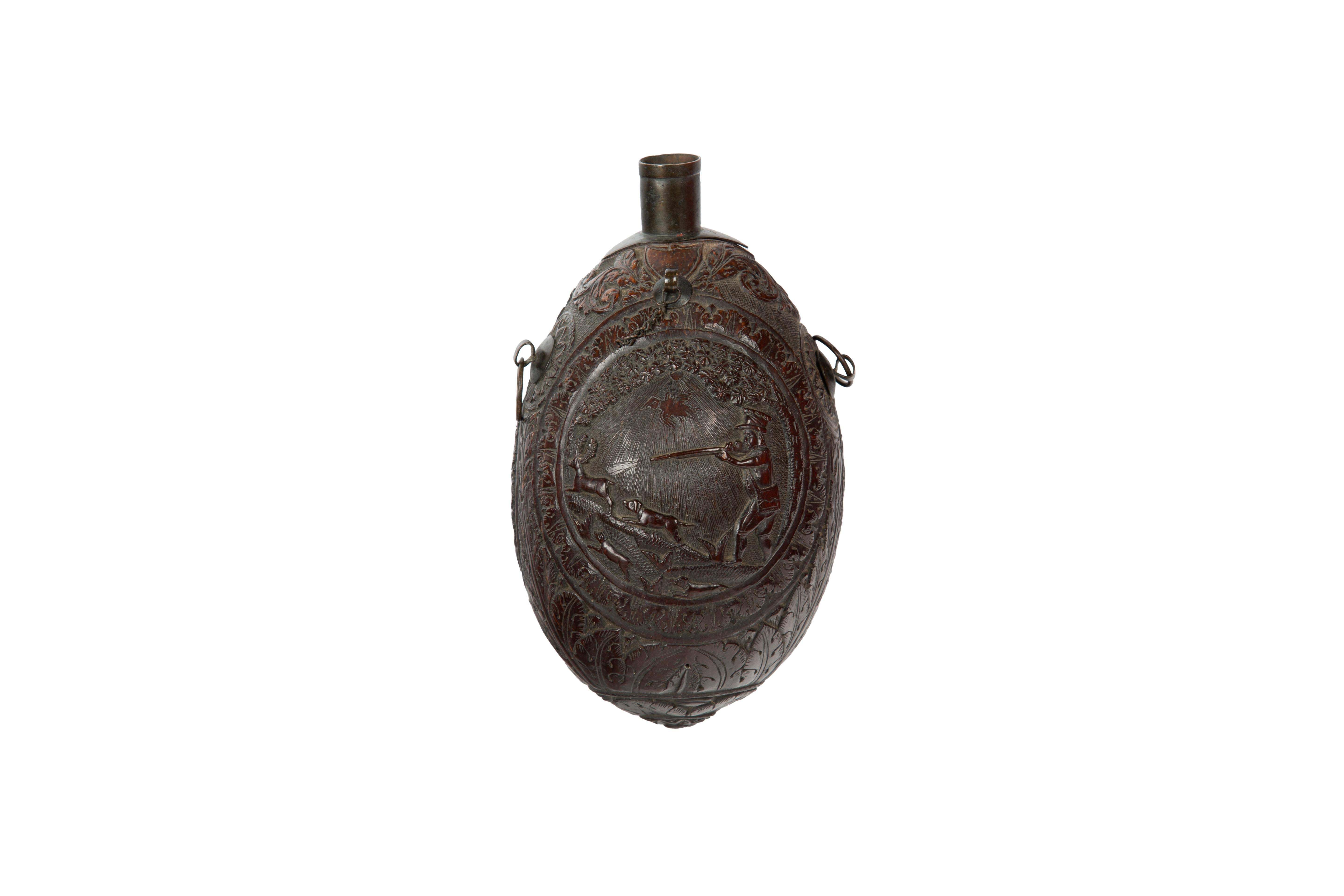 This 18th century carved bugbear coconut flask is a fascinating artifact that showcases both artistic craftsmanship and historical significance. The flask is adorned with a relief-carved hunting scene, depicting a gentleman with a rifle, accompanied