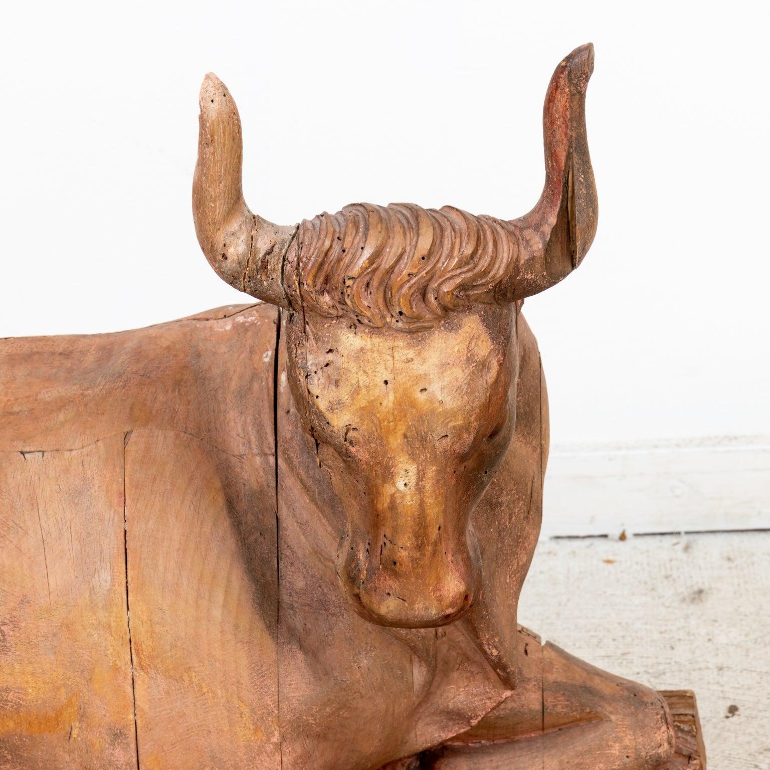 Circa 18th century decorative carved wooden figurine of a seated cow on a plinth. Please note of wear consistent with age including patina, chips, and minor wood loss.
 