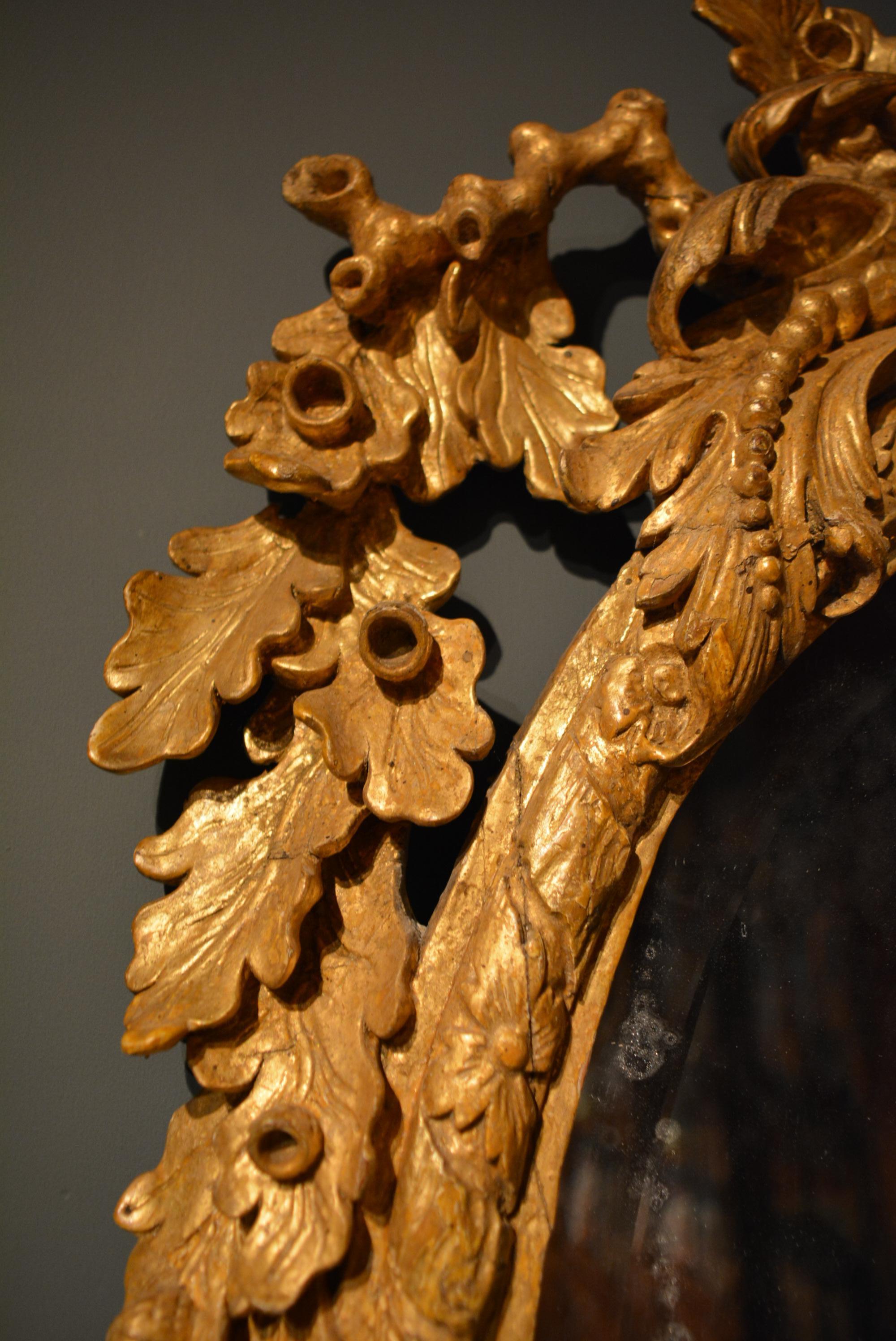 A George II carved giltwood mirror of unusual form with shell cresting supported by trailing oak branches and leaves.