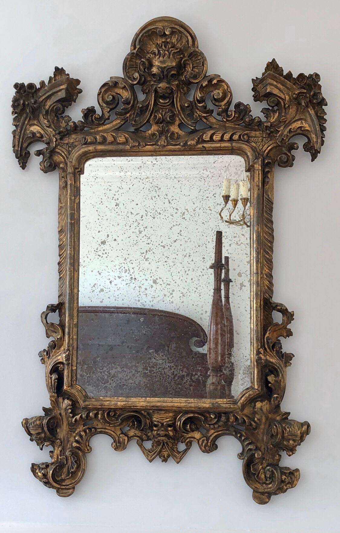 Dieser italienische Spiegel aus vergoldetem Barockholz aus dem 18. Jahrhundert hat ein theatralisches Gesicht an der Spitze mit Schwänzen, die zu den Füllhorn-Ecken fließen. Der kühne Rahmen ist mit klassisch geschnitzten Schnörkeln versehen. Die