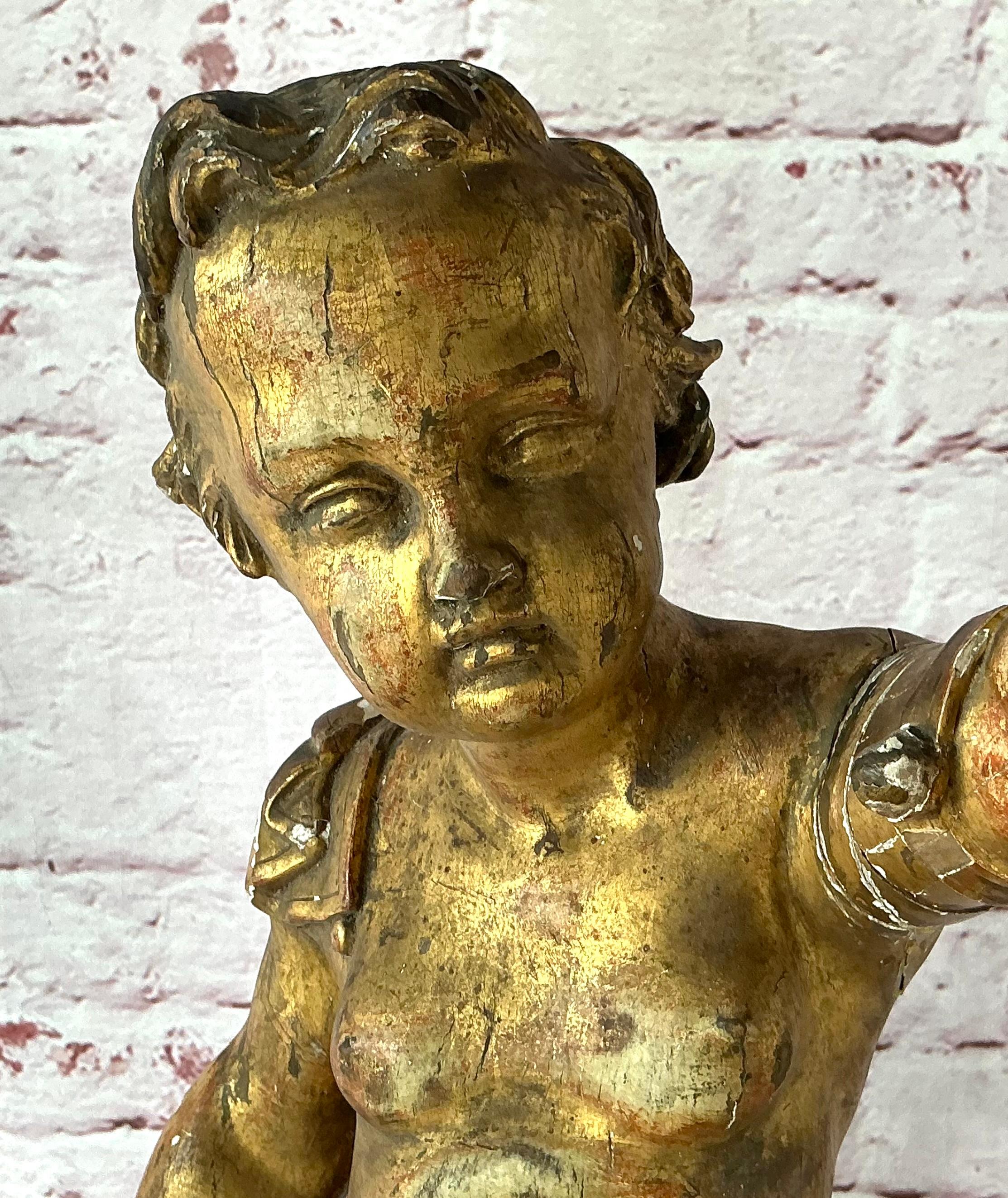18th Century Baroque Carved Giltwood Putti Figure on Stand. The figure is depicted in a dynamic pose, with one hand raised heavenward and the other lightly grasping drapery at the waist. Carved with lively movement and a naturalistic sense of form,