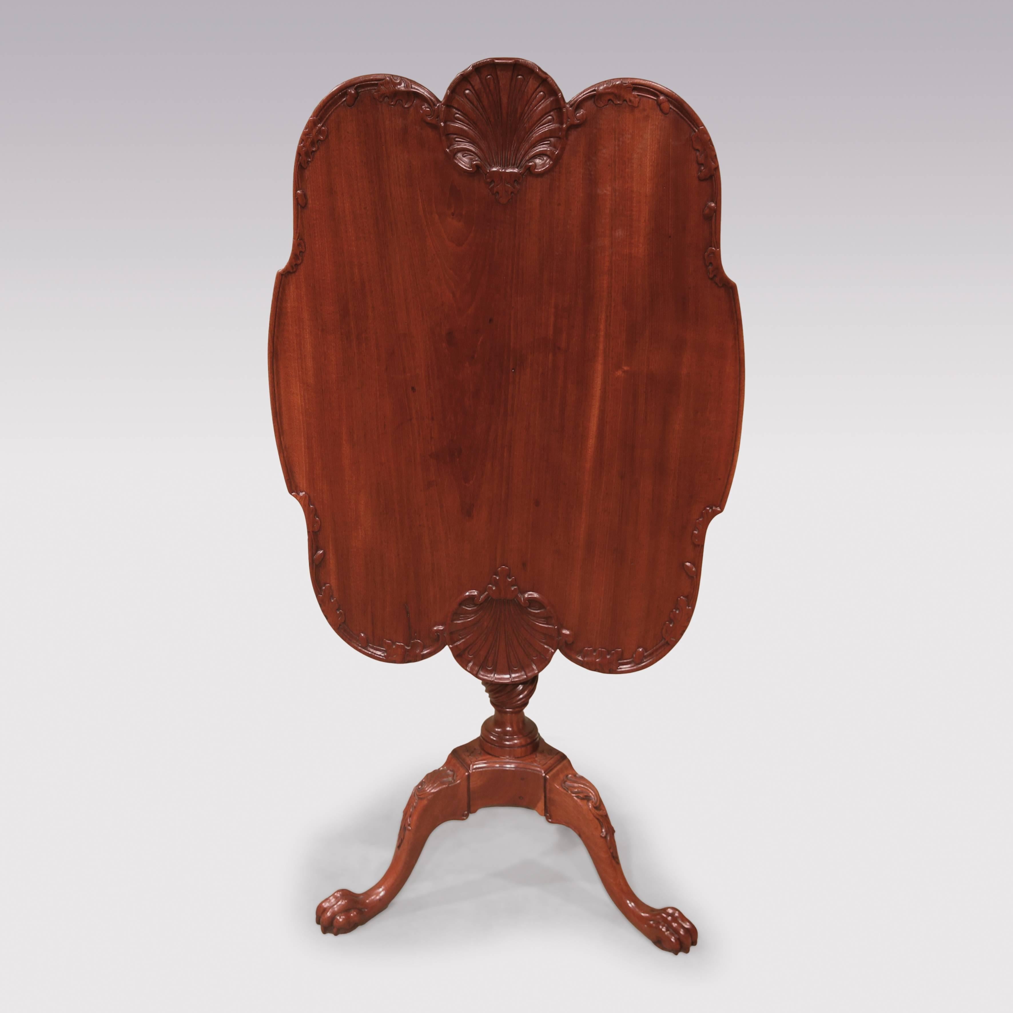 An unusual mid-18th century figured mahogany dish-top tripod table of rounded rectangular form, carved with oak leaves and acorns and scalloped shells to the sides, raised on fluted gun-barrel and spiral twist stem supported on leaf scrolled, carved