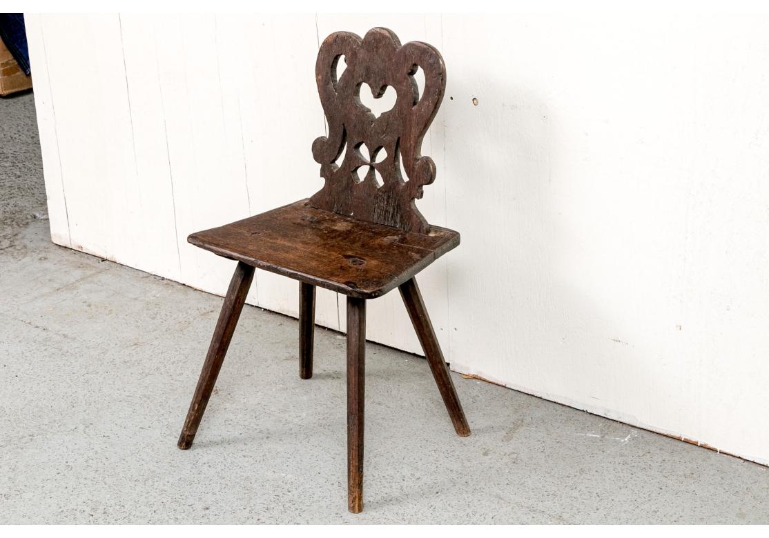 A small scale dark wood side chair with a separately made carved openwork back in a scrolled design with a heart and flower. The back has extensions on the bottom that are inserted into a slot at the back. Each has a hole for an original attachment