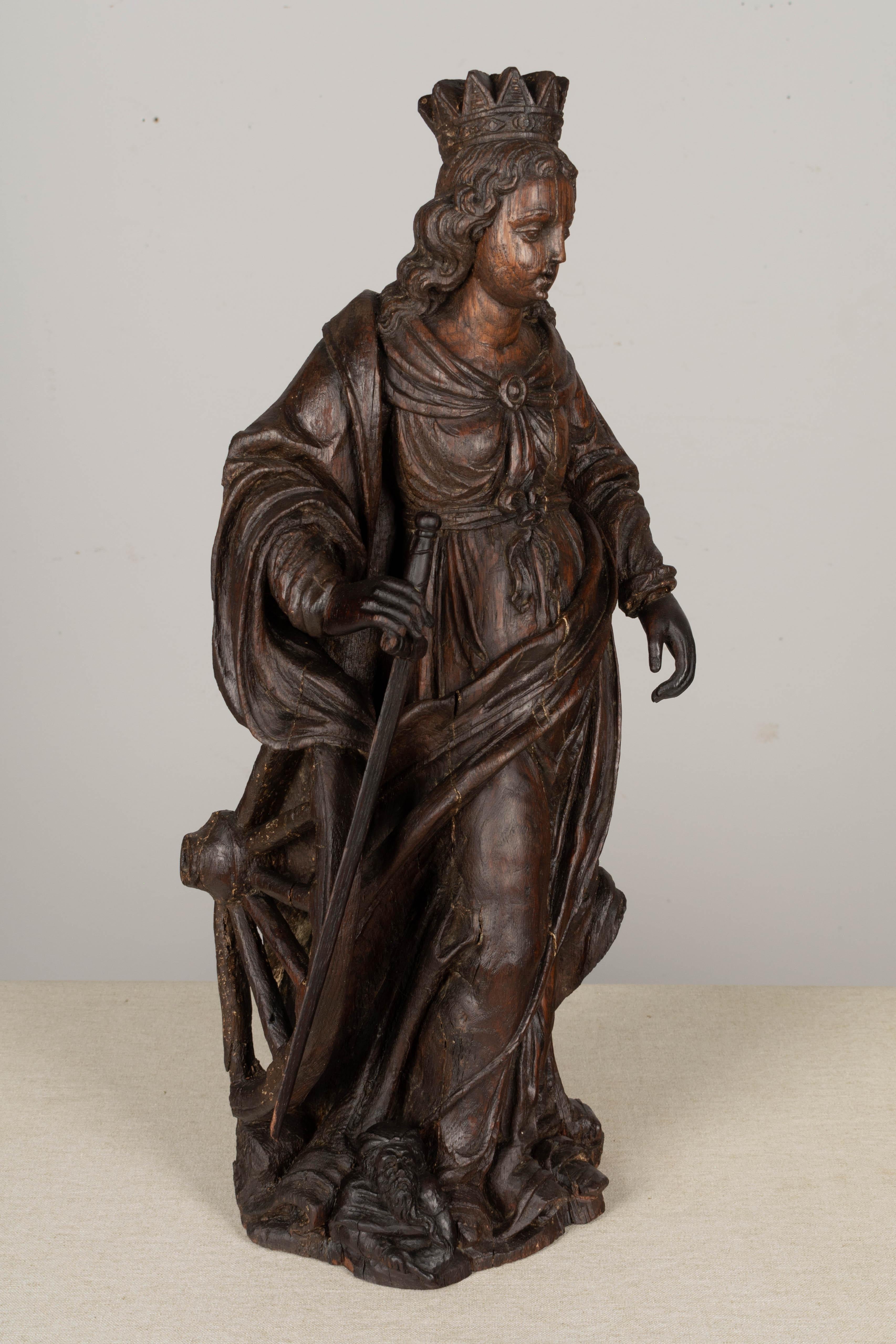 An 18th century carved oak statuette of Saint Catherine of Alexandria, probably South German, depicting a finely carved figure in pooling robe with bow cinched at the waist, scroll carved hair surmounted by a crown, with sword at hand, a wheel at