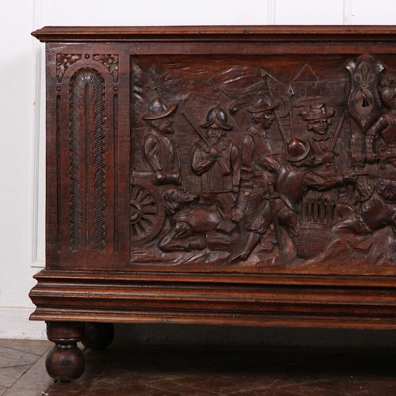A large and imposing Italian or possibly Spanish coffer in walnut featuring a minutely-detailed carved battle scene on the front, flanked by architectural carved arched panels, the sides also with carved geometric paneling. Original wrought iron