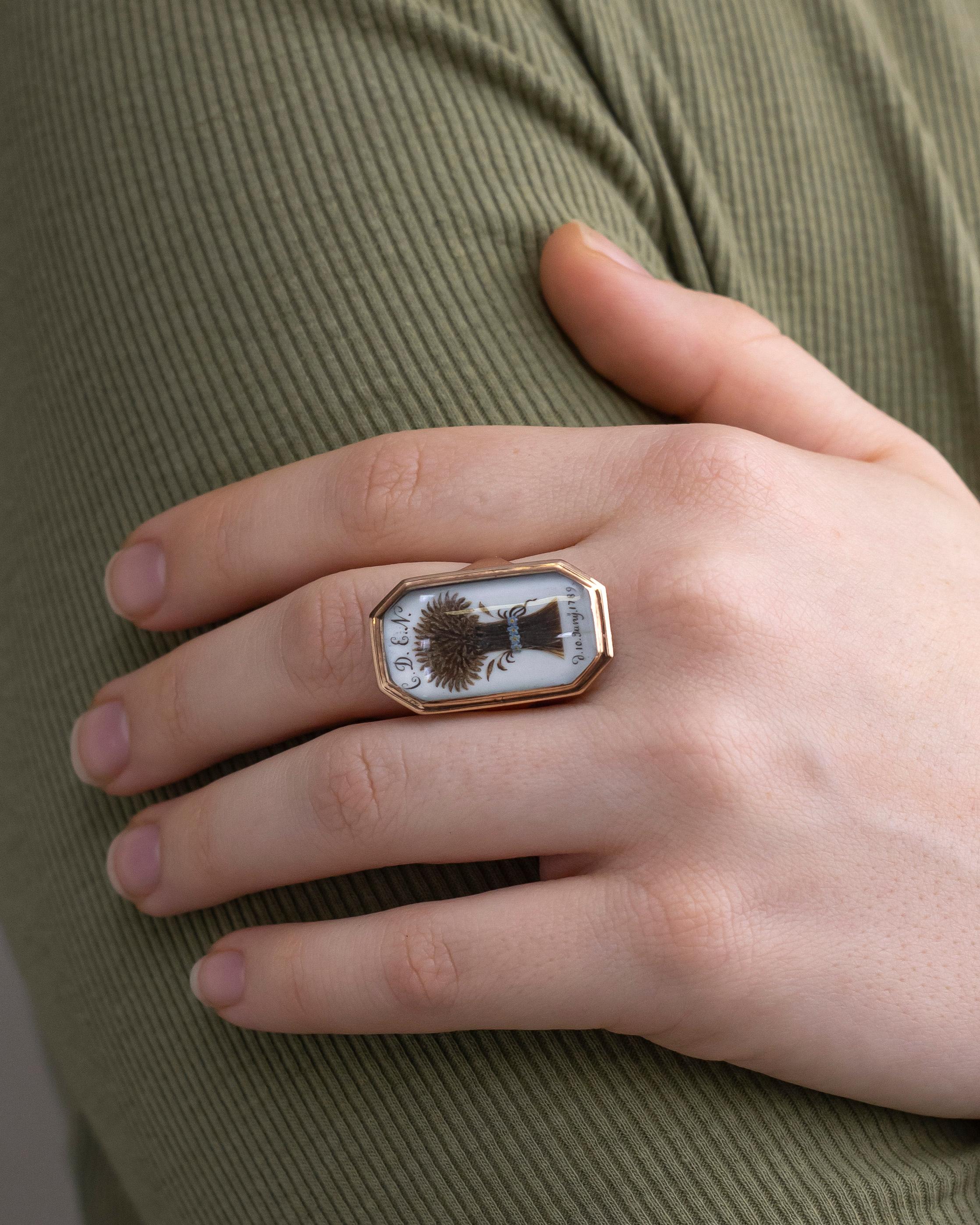 This unusual mourning ring is not only unique, but in really lovely condition for its age. The elongated octagonal fronted ring has a frame of 9 karat yellow gold which encloses a fine sliver of ivory that is a base for a fine hairwork wheatsheaf