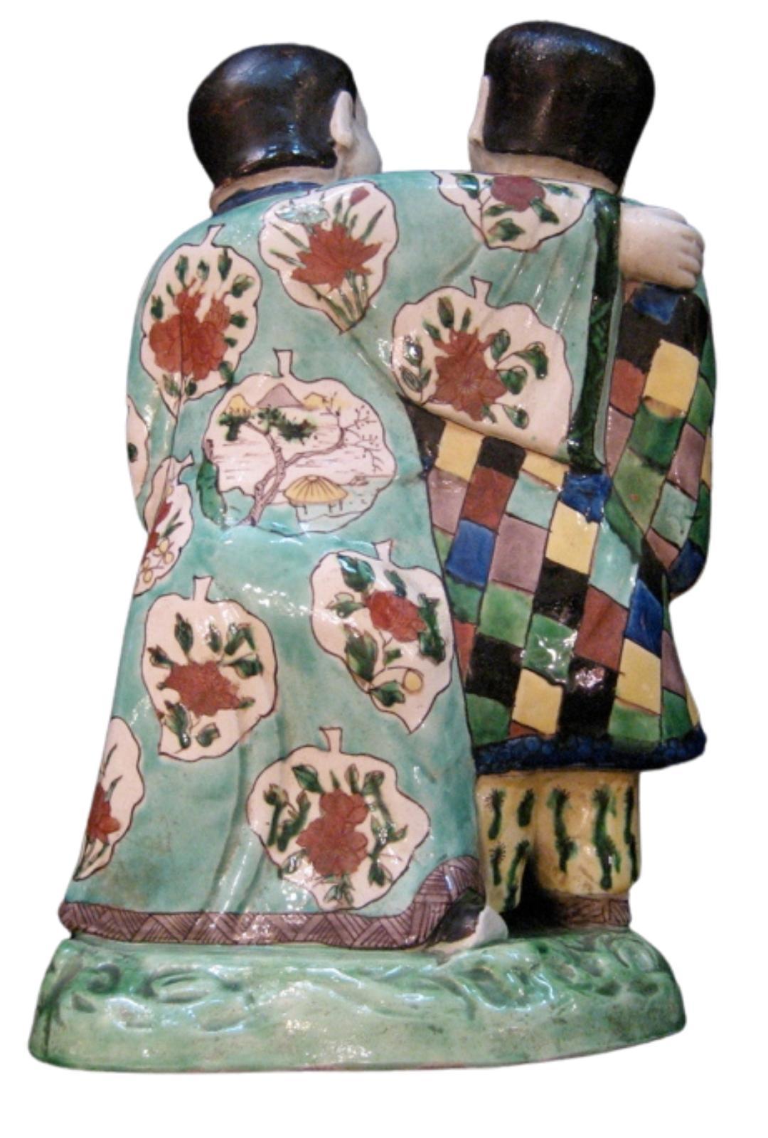 An 18th century Chinese export porcelain group of two men, tongue out in hilarious conversation.
The man holding a vase is clad in chequered robe over yellow trousers,
his friend has his arm around his shoulder and his robe is adorned with