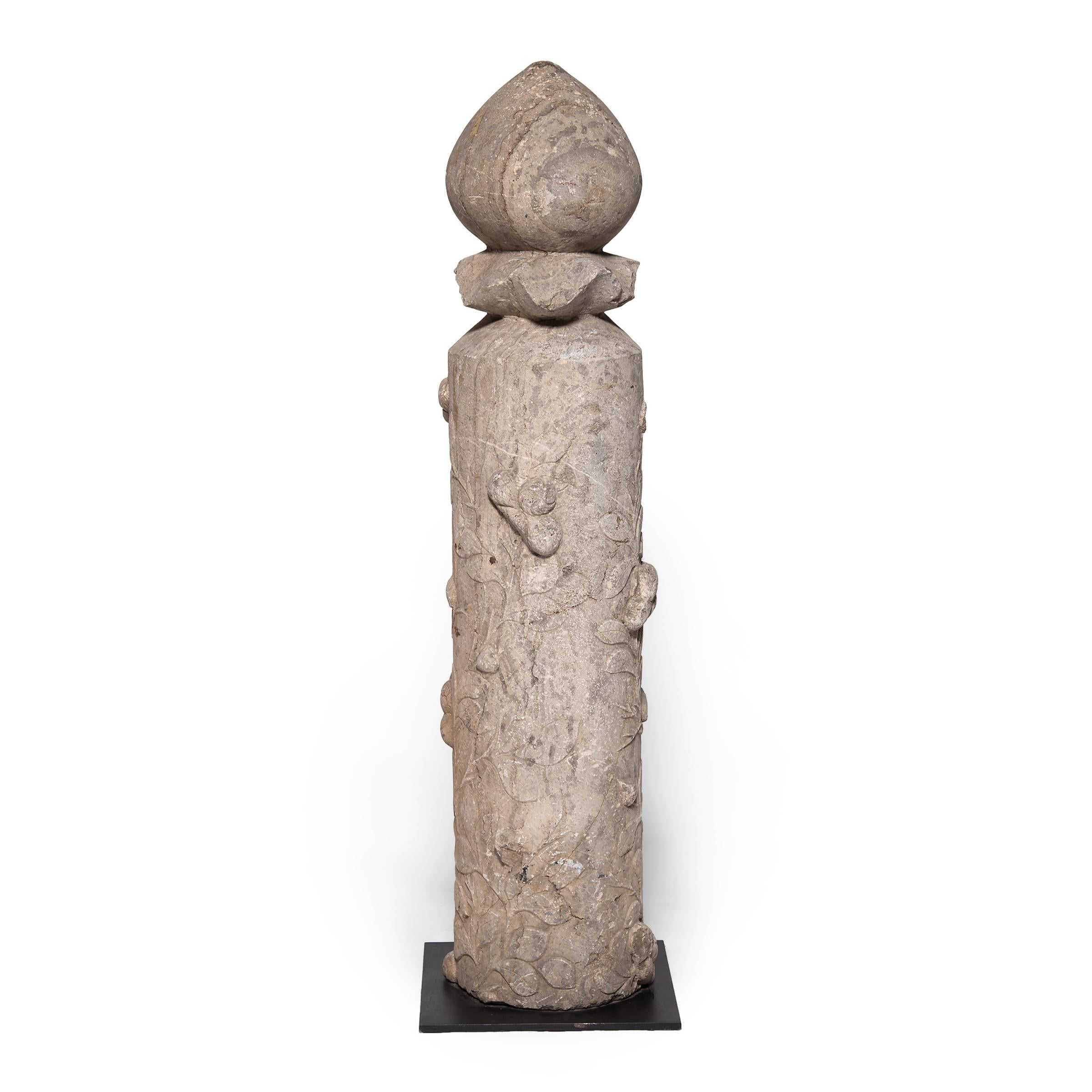 This sculptural stone post was hand-carved in the 18th-century from a solid block of limestone. The column is crowned with a lotus bud - a symbol of purity and perfection. Trailing vines carved in low relief wrap around the base, dotted with raised