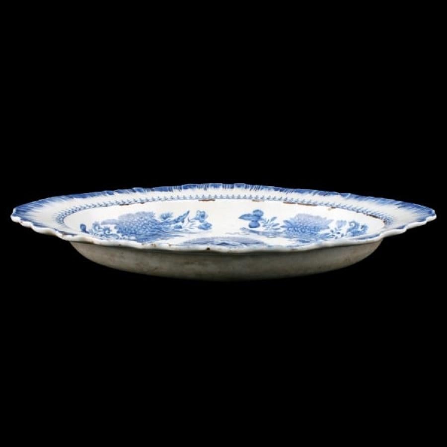 An 18th century Chinese porcelain oval shaped deep dish.

The dish has a shaped and writhen edge, a white background and is decorated with flowers, foliage and scrolls in blue.

The back of the dish is white with a ground base.

The dish is in