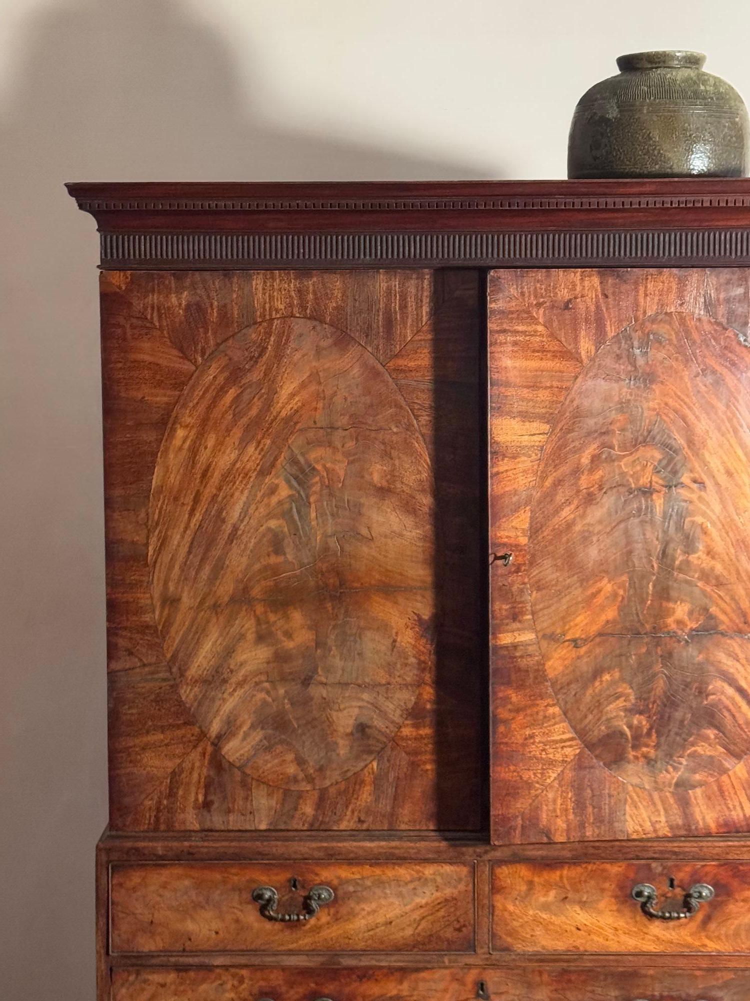 A fine quality George III mahogany linen press in the manner of Thos Chippendale C.1760, the flush fronted door panels with cross banded ovals, a chatting cornice with fluting and dentil moulding. Inside the red washed carcass has four slides for