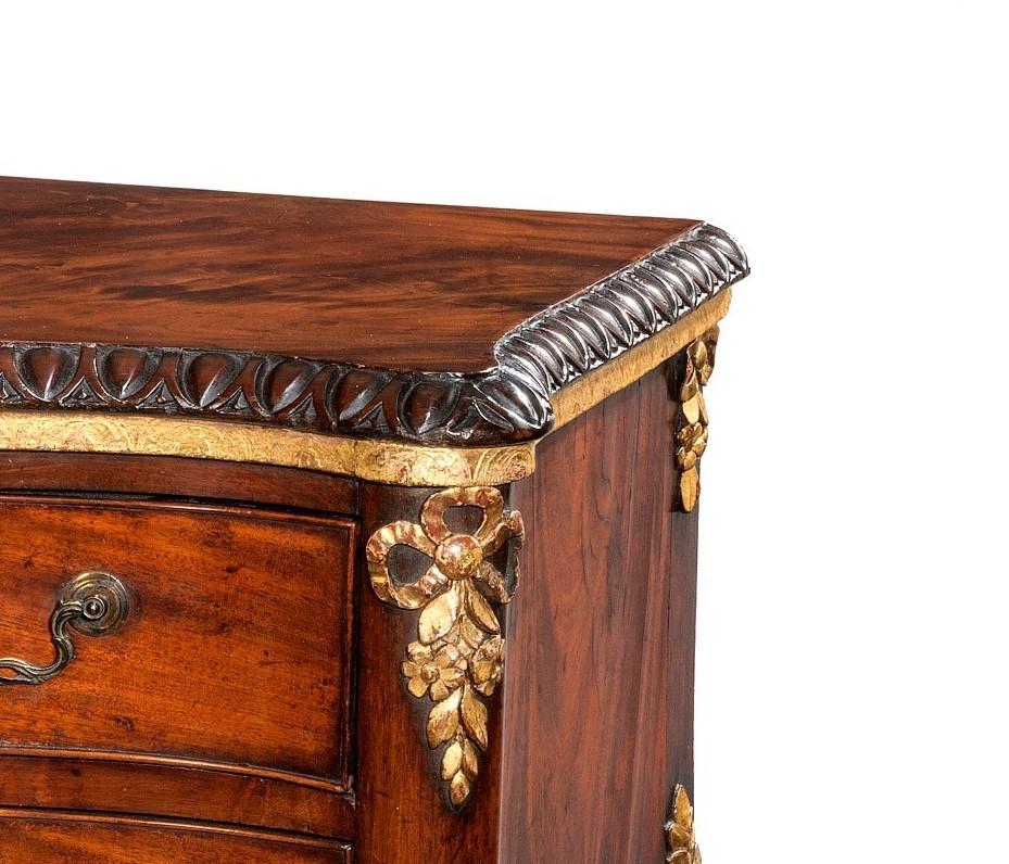 18th century mahogany and parcel-gilt commode chest of drawers. The shaped rectangular serpentine top having a carved edge top above two drawers. Cascading carved giltwood swags as an apron to the sides and front. This article was constructed in