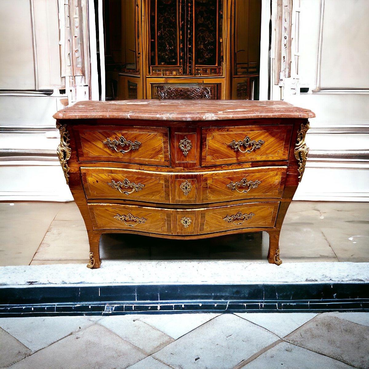 We present you with this rare chest of drawers hailing from the Louis XIV Regency era in the 18th century. It has a gracefully curved facade which unfolds with four drawers arranged in three tiers as well as two asymmetrical drawers beneath its