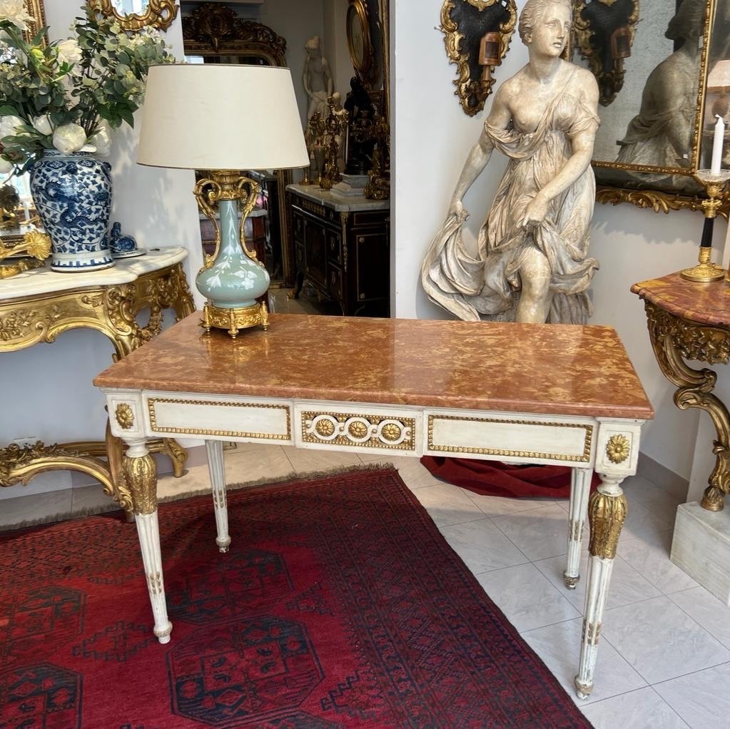 Te presentamos esta rara consola del siglo XVIII, de estilo Luis XVI, fabricada en madera pintada (réchampi en francés) y dorada. 

Presume de una encimera de mármol rosa de tonos delicados, finamente tallada a la perfección. El soporte central está