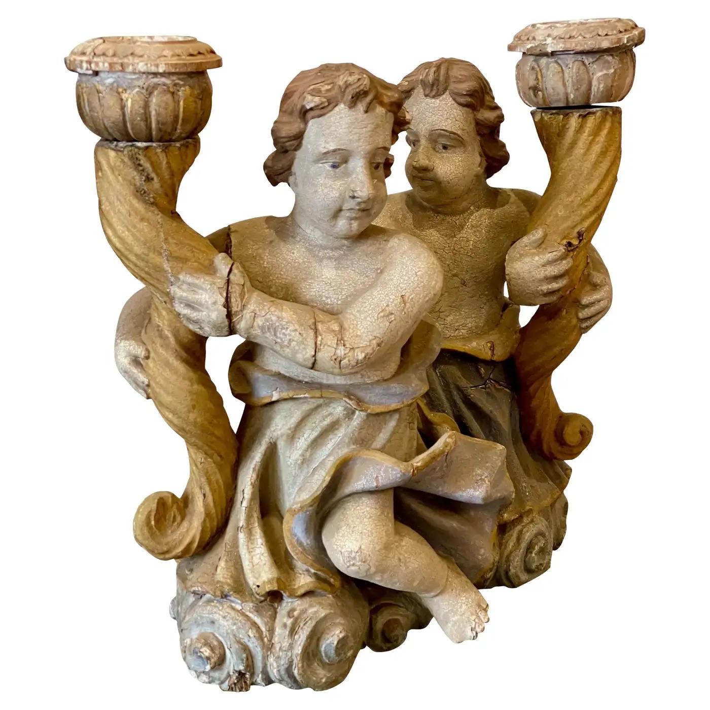 Continental carved and polychrome decorated cherub candle holders, second quarter 18th century, each retaining original paint, and depicting two putti supporting a stylized cornucopia carved standard, and rising on a billowing clouds form base, 16