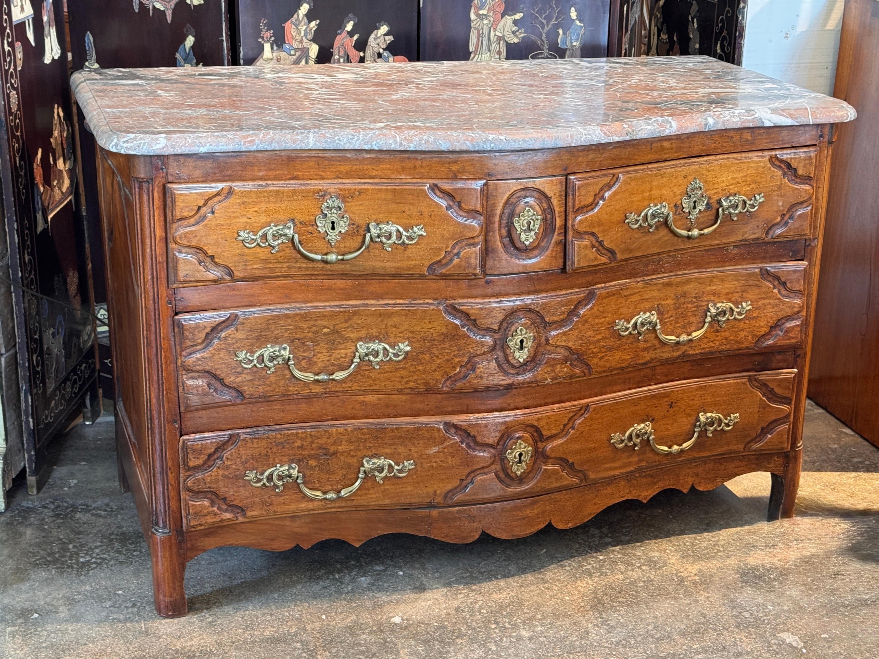 18th century Continental commode featuring a serpentine front and richly molded drawer fronts, topped with an expressive veined marble surface. The case is detailed with gilt bronze hardware and retains a charming hidden center drawer. Dovetailed