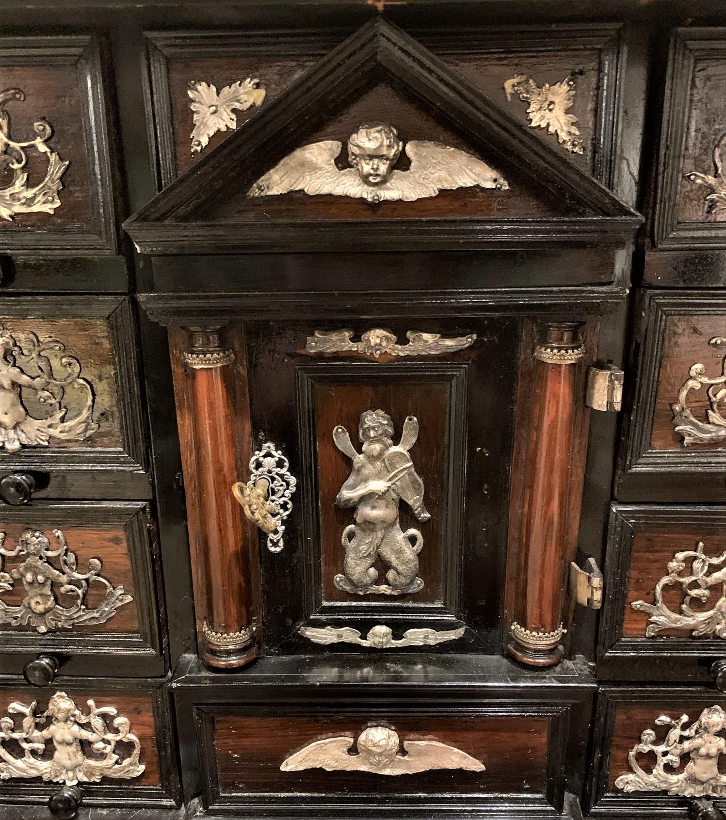 Important 18th century Continental ebonized trinket cabinet with a lift-top compartment having rosewood inlays. The doors open to reveal painted inset panels and multiple fitted drawers adorned with silver filigree mounts. The paneled sides