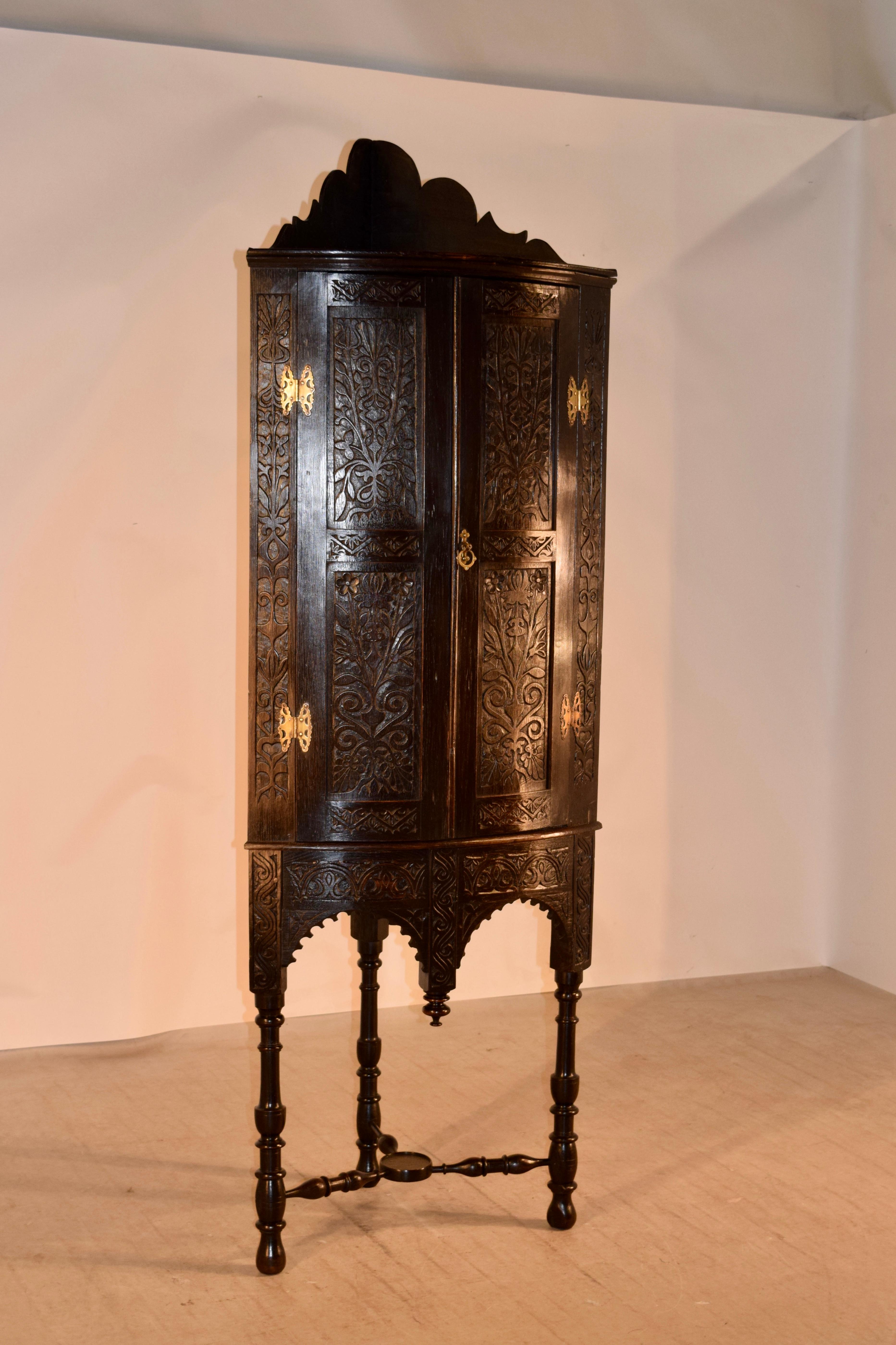 18th century oak corner cupboard on stand from England. The top molding is wonderfully scalloped and forms a lovely background for a top shelf. This is over a molded edge and a convex shaped front continuing two heavily carved decorated doors,