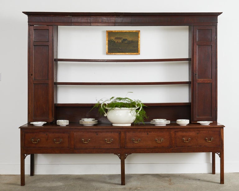 Imposing late 18th century country English Georgian period welsh dresser with cupboards and plate rack. Crafted from oak with a corniced top and supported by tall, narrow locking cupboards on each side. The storage cabinets are conjoined by three