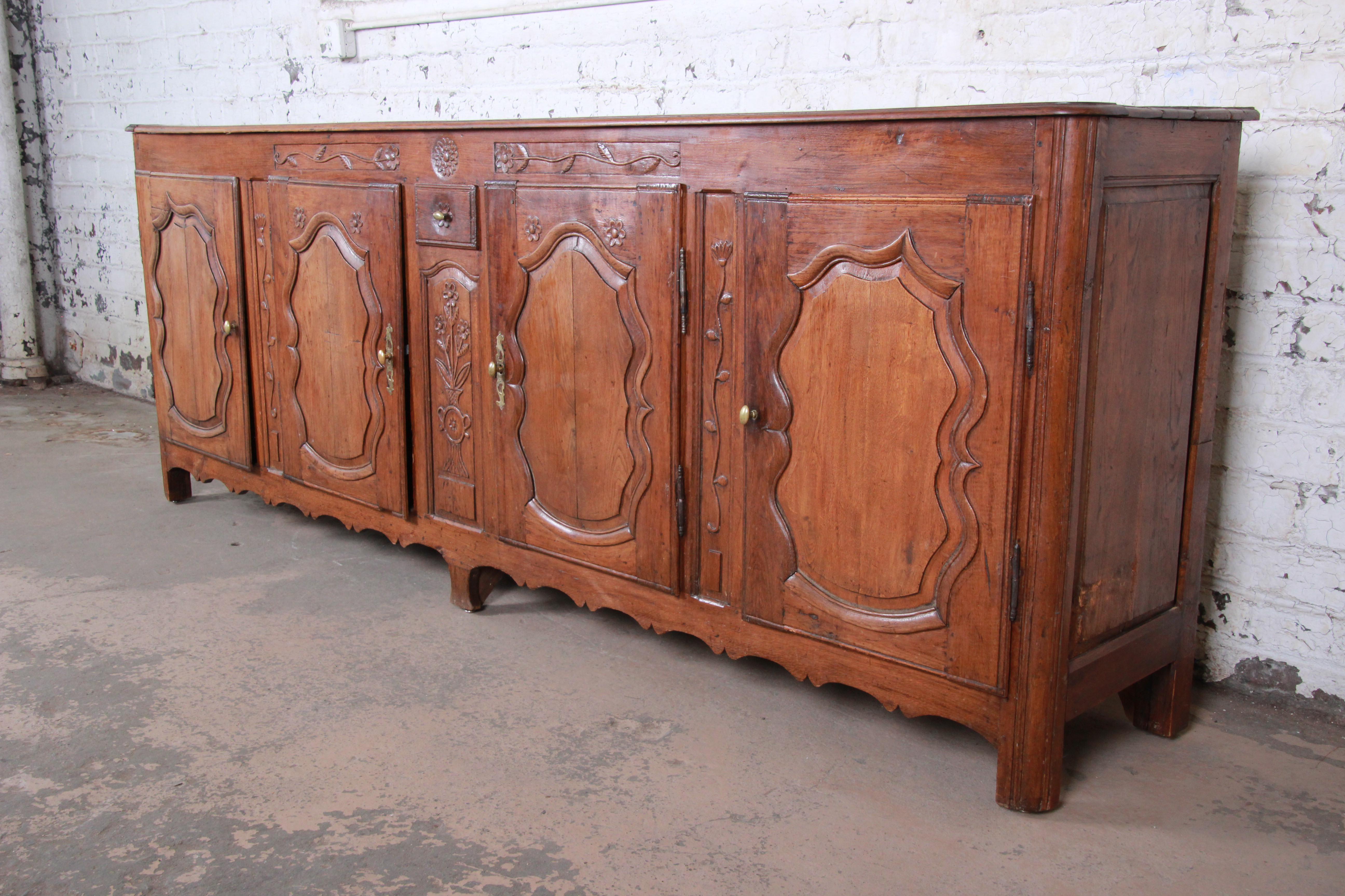 An outstanding monumental 18th century French Provincial sideboard. The sideboard features solid walnut construction and gorgeous carved wood details. It offers ample storage, with four cabinets with adjustable shelving behind four carved doors and