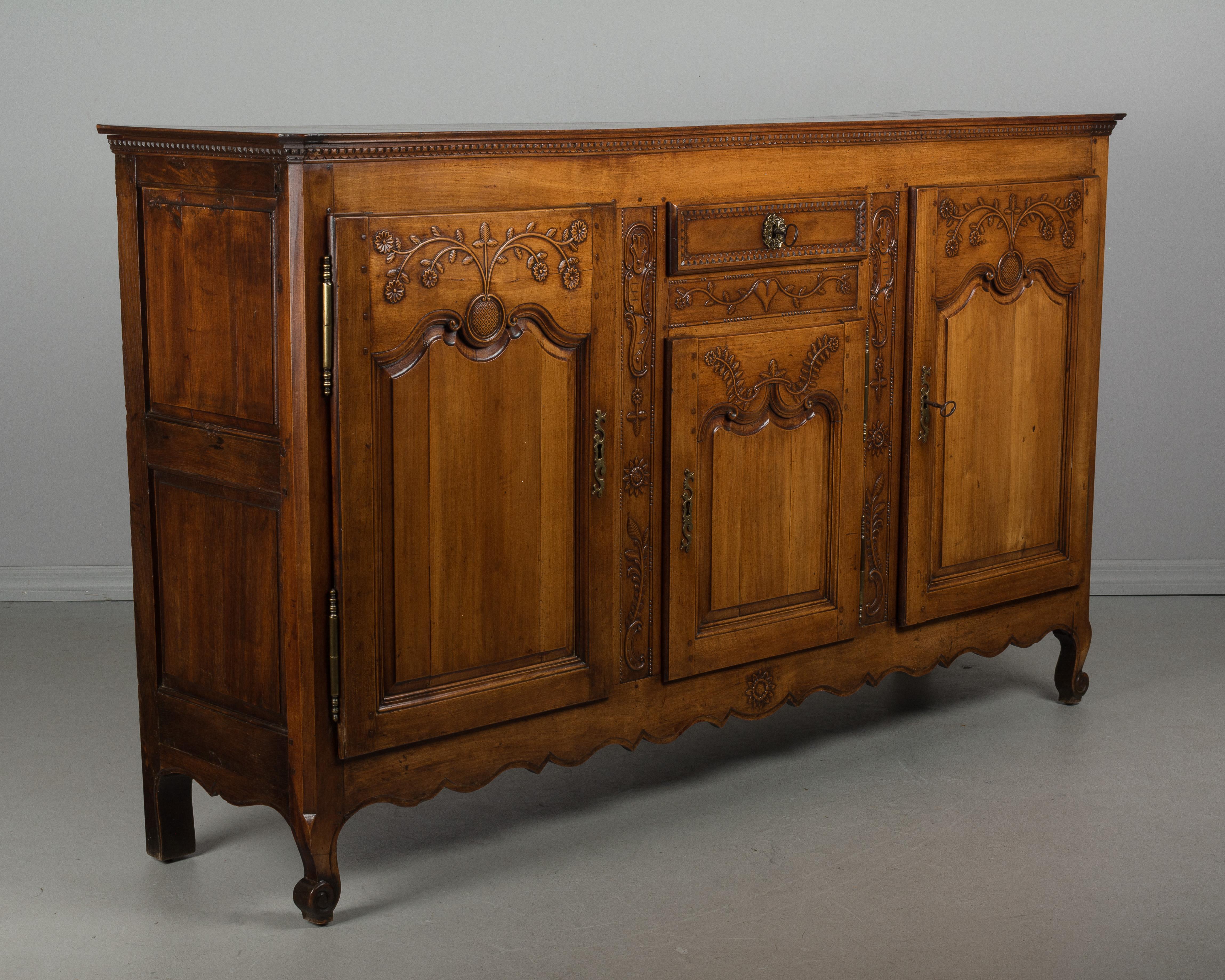 A late 18th century Country French enfilade or sideboard from Picardie (Northern France) made of solid cherry with waxed patina. Beautiful hand-carved details include flowering vines and sunflowers on the raised panel doors and decorative carved