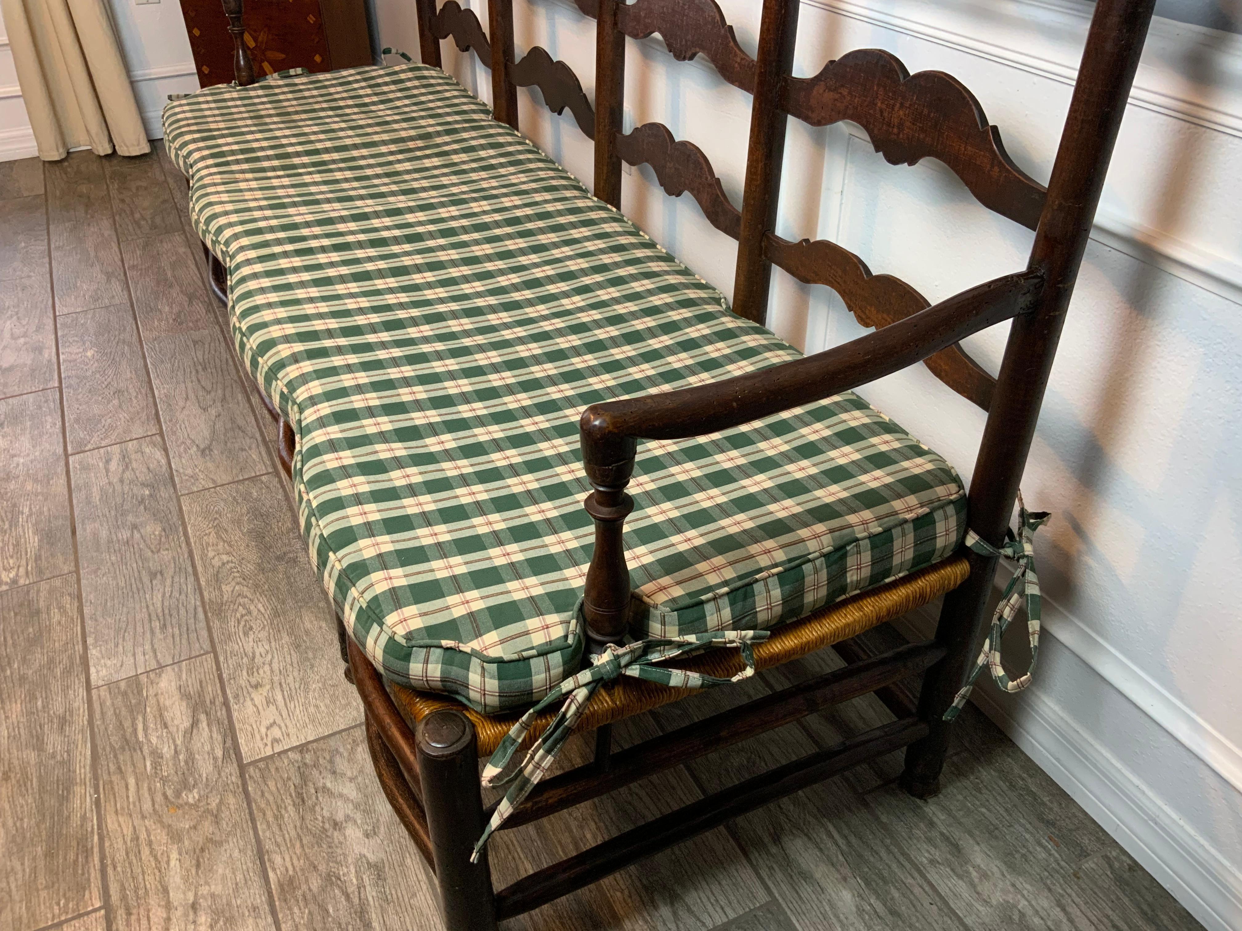A very nice 18th century country French four seat ladder back bench. The frame looks to be made of Maple and Ash with fruitwood back splats. A new rush seat has been applied along with a custom made cushion with ties. Seat height is 16.75 with the