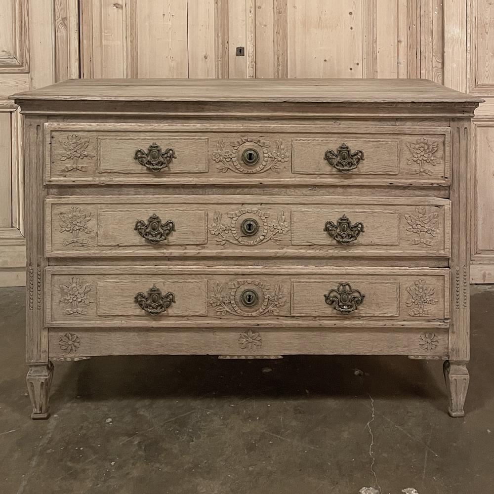 18th century Country French Louis XVI Neoclassical Commode in Stripped Oak exudes a timeless elegance, featuring hand-carved detailing across the drawer facades and cast bronze neoclassical pulls and keyguards. The classical architecture recalls the