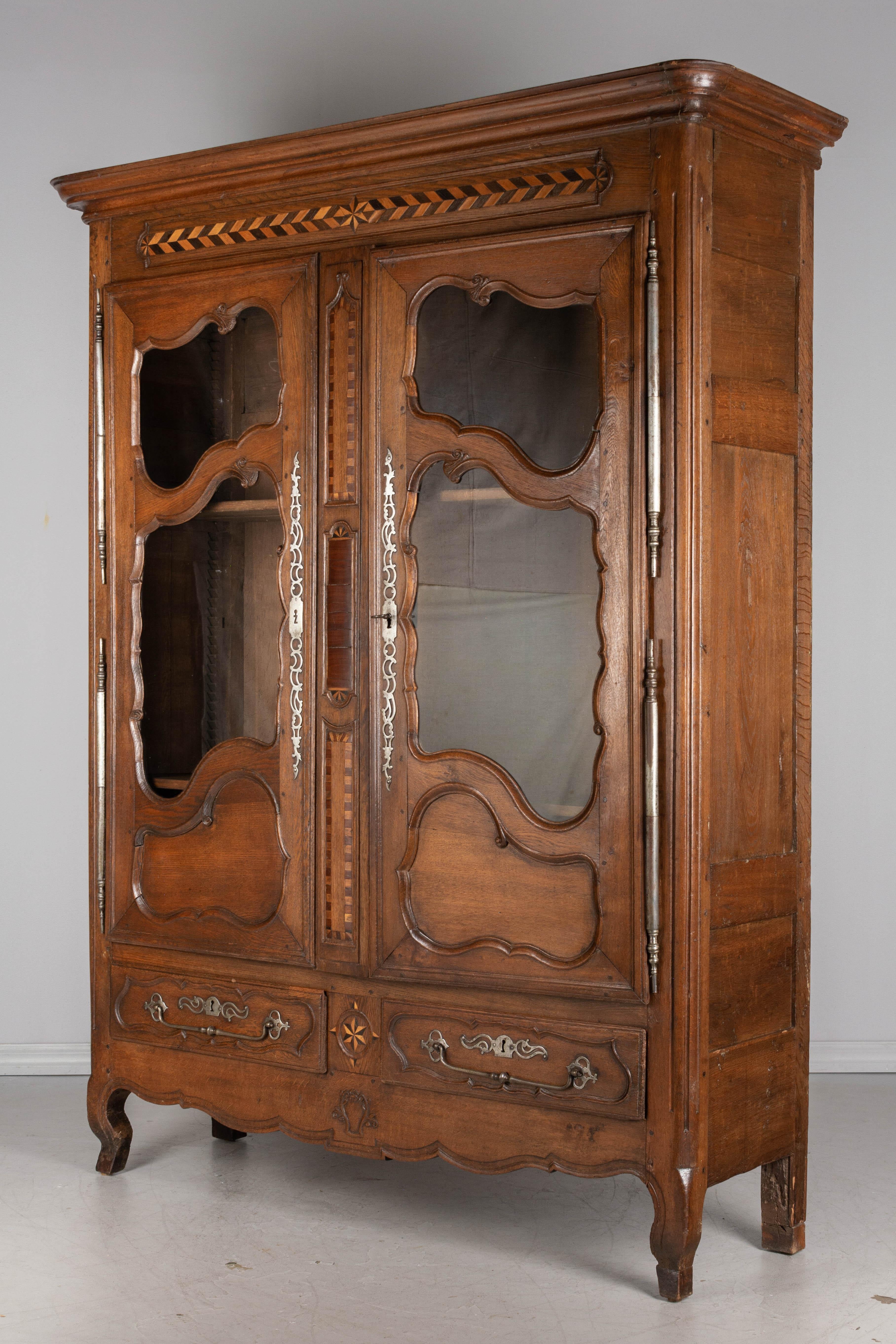 An 18th century country French armoire, or vitrine, from Alsace made of solid oak with inlaid mahogany and cherry Marquetry details. Original iron hardware with long decorative escutcheons on the doors, wide drawers pulls and large heavy hinges.