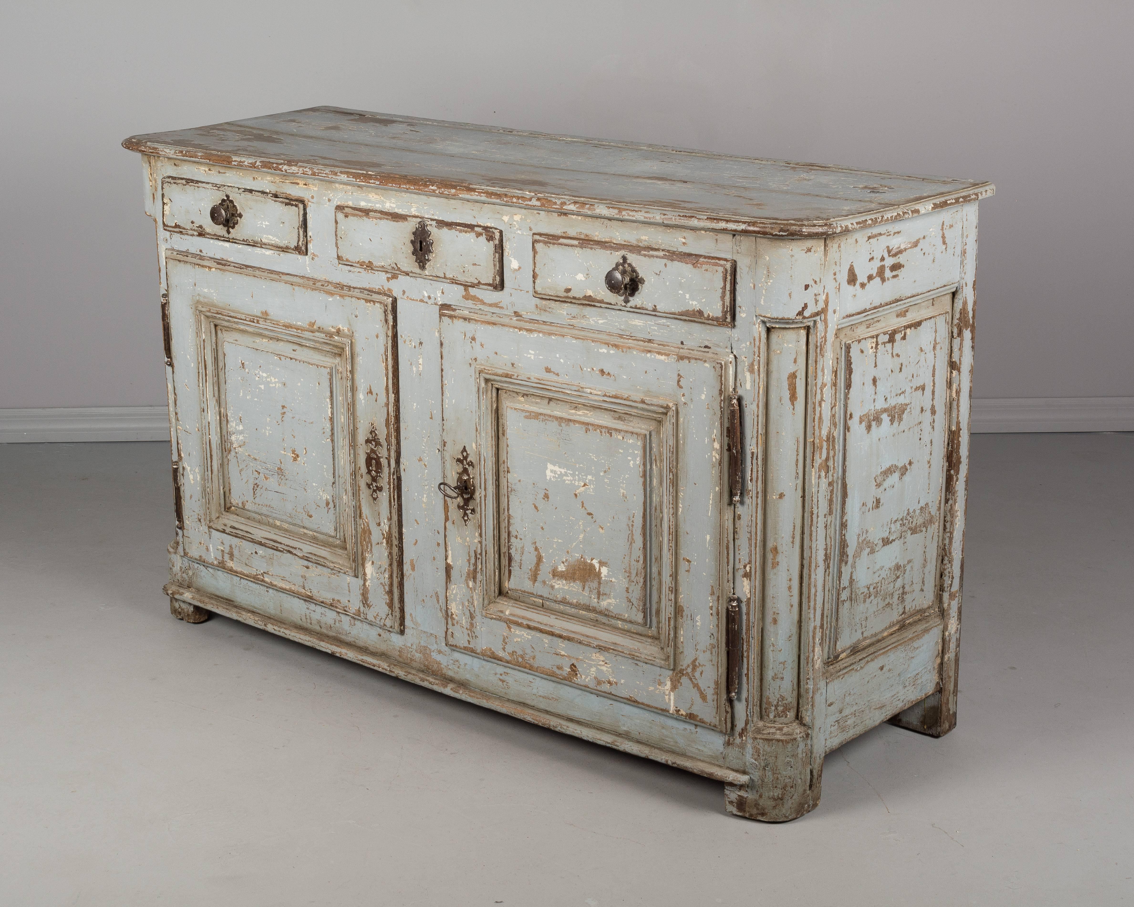 A large 18th century Country French buffet made of solid oak with newer distressed blue grey painted finish. Three dovetailed drawers. Ample storage provided, opening to a single shelf. Original hardware. Working lock and key. Old restoration on