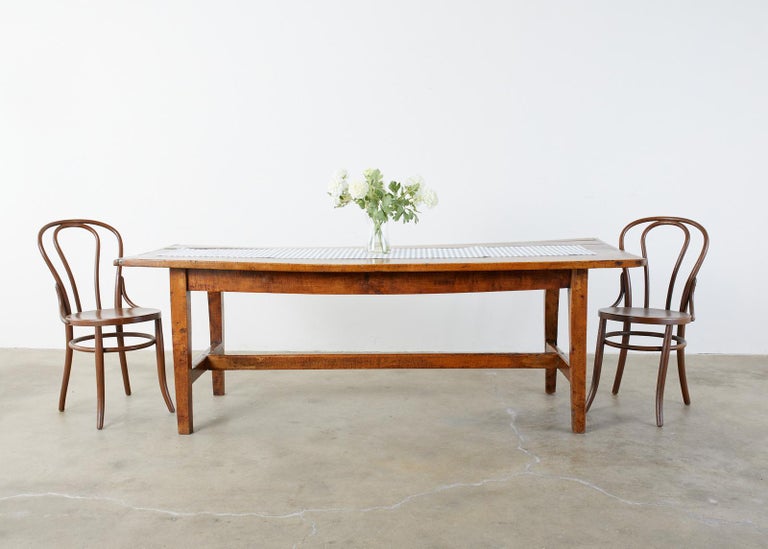Rustic late 18th century country French provincial farmhouse dining table constructed from warm toned fruitwood. The top is rectangular crafted from three planks having breadboard ends. Supported by a trestle style base having thick tapered legs
