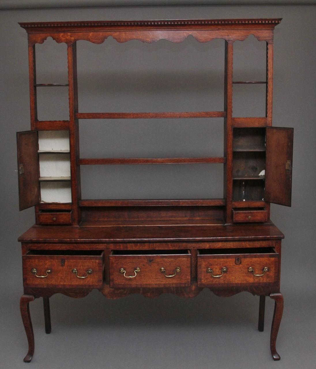 A lovely quality 18th century country oak dresser and rack, having a moulded edge cornice on the rack with dentil moulding and a decorative shaped frieze below, there are three shelves in the centre and a cupboard at each side with a single drawer