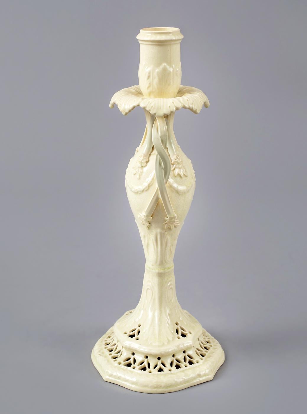 Early elegant creamware candlestick, the double strap handles are twisted and end in leaf terminals, the bobeches supported by a shaped leaf drip tray, the vase shaped body on a pierced base. The piercings are stylized flower heads and leaves.